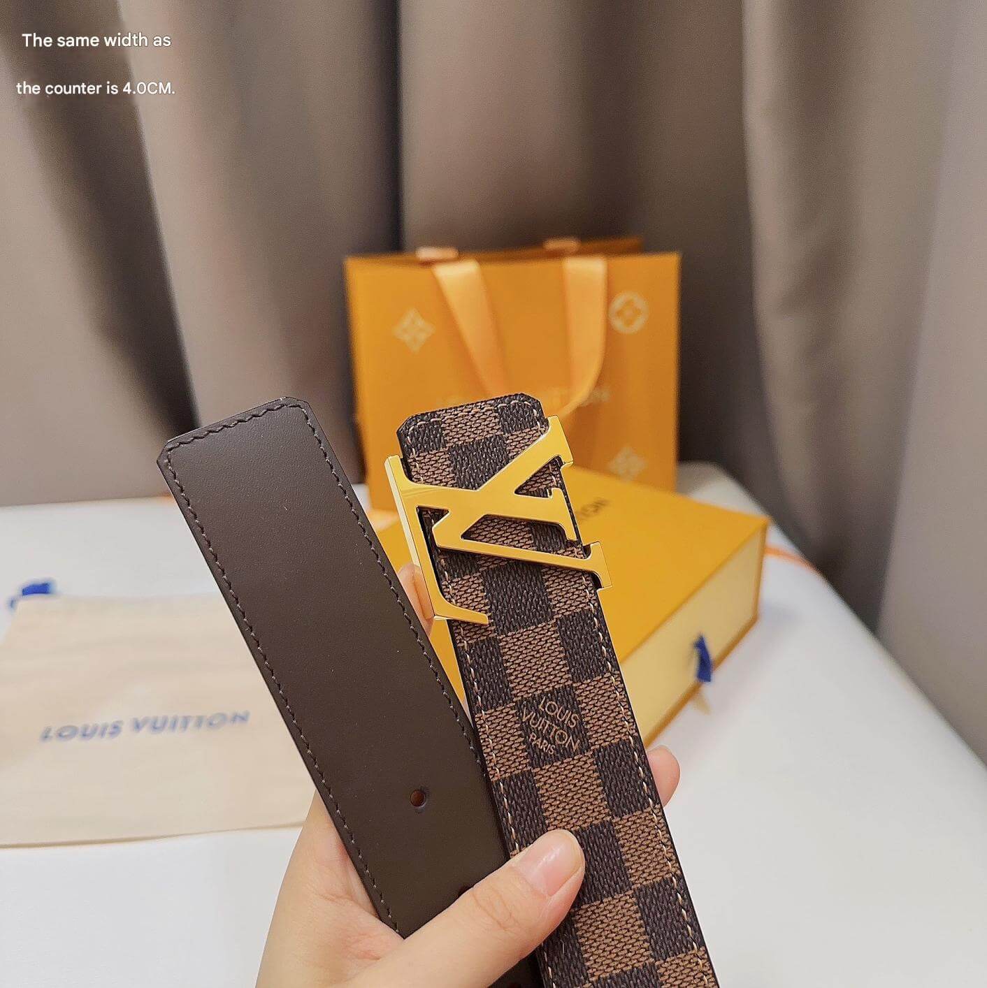 Louis Vuitton belt with checkered pattern held by a hand, with brand box in the background.