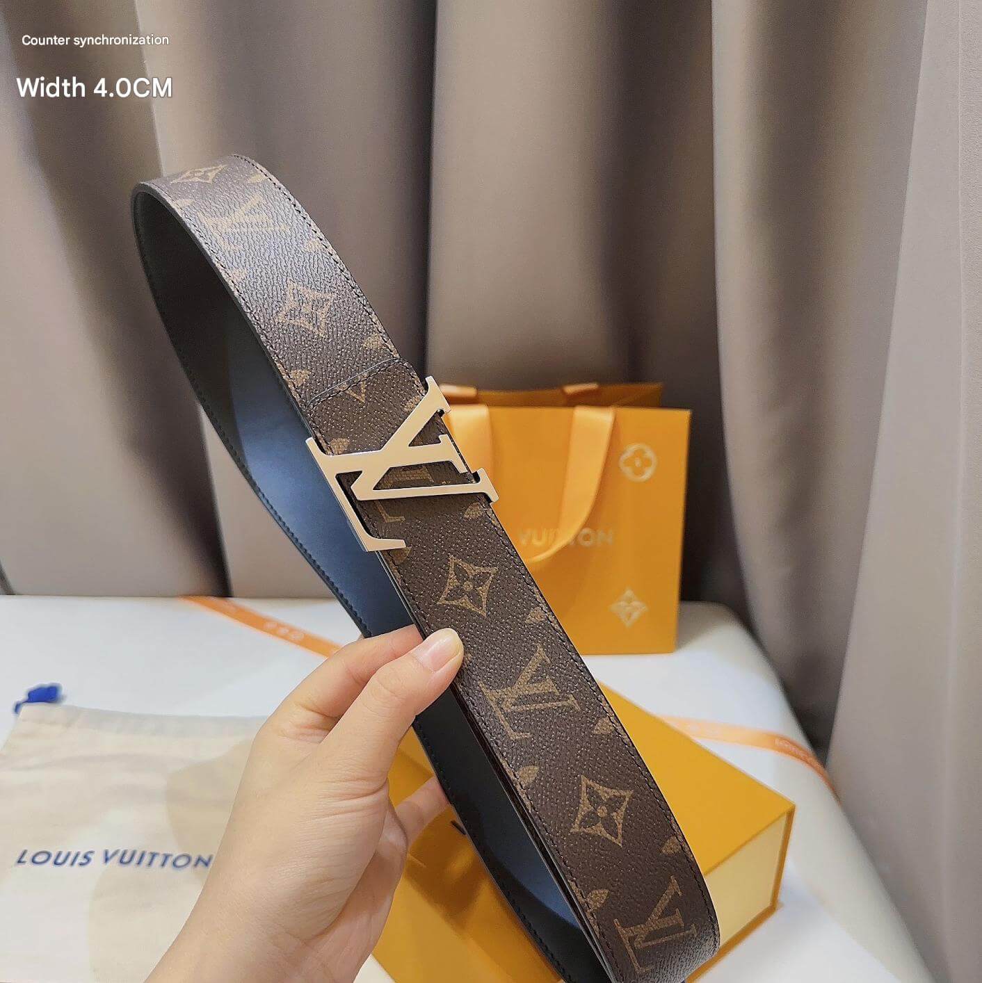 Louis Vuitton belt held by a hand with a branded box and bag in the background.