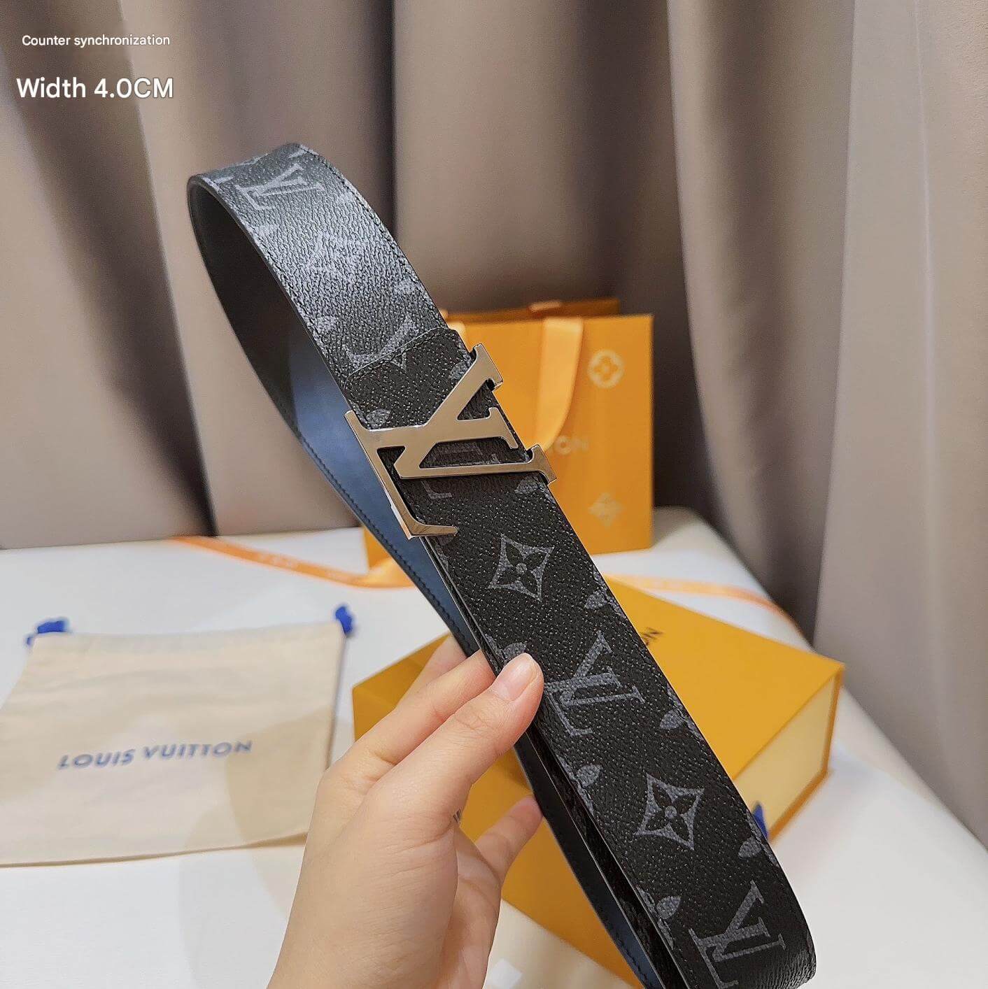 Louis Vuitton belt with monogram pattern held by a hand, with brand packaging in the background.