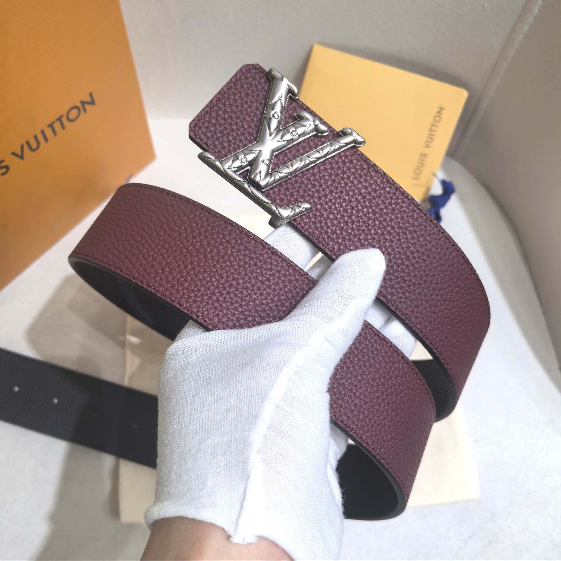 Purple belt with silver buckle held by a gloved hand, with a Louis Vuitton box in the background.