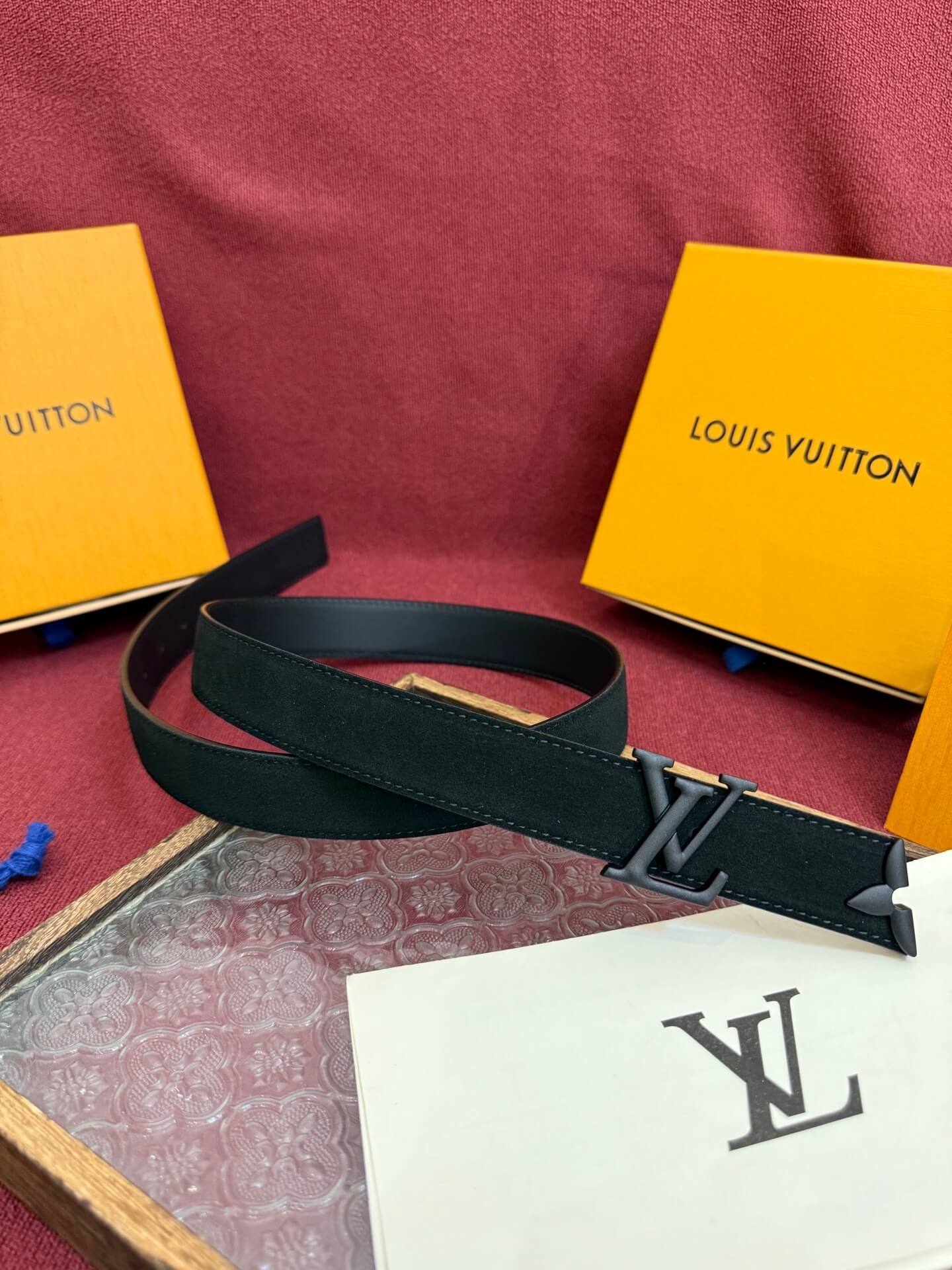 Black belt with Louis Vuitton logo on a red surface with brand boxes in the background