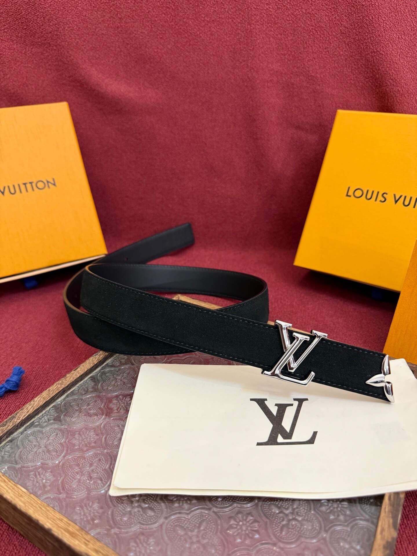 Black Louis Vuitton belt with monogrammed paper and orange boxes in the background.