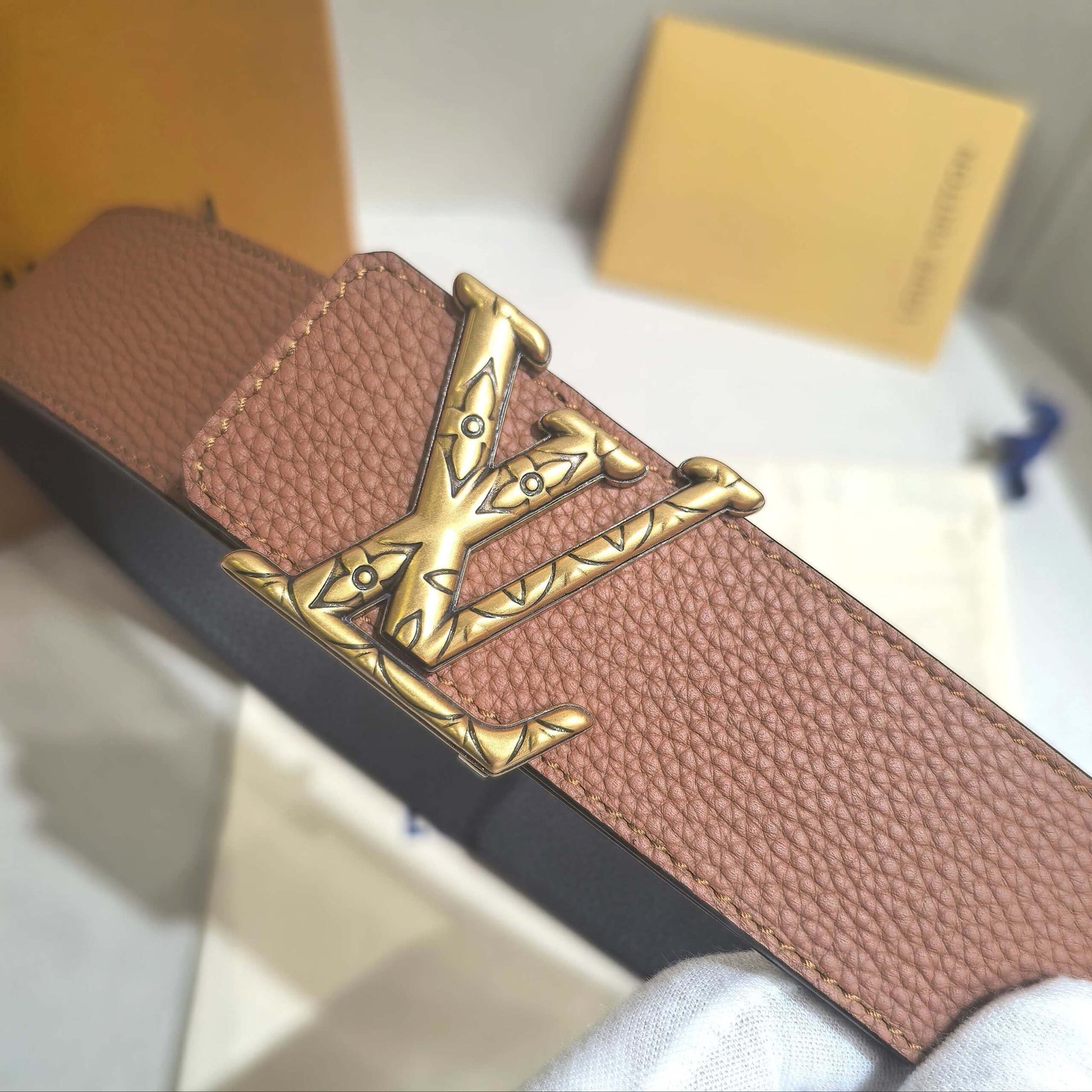 Brown leather belt with gold buckle on a white surface