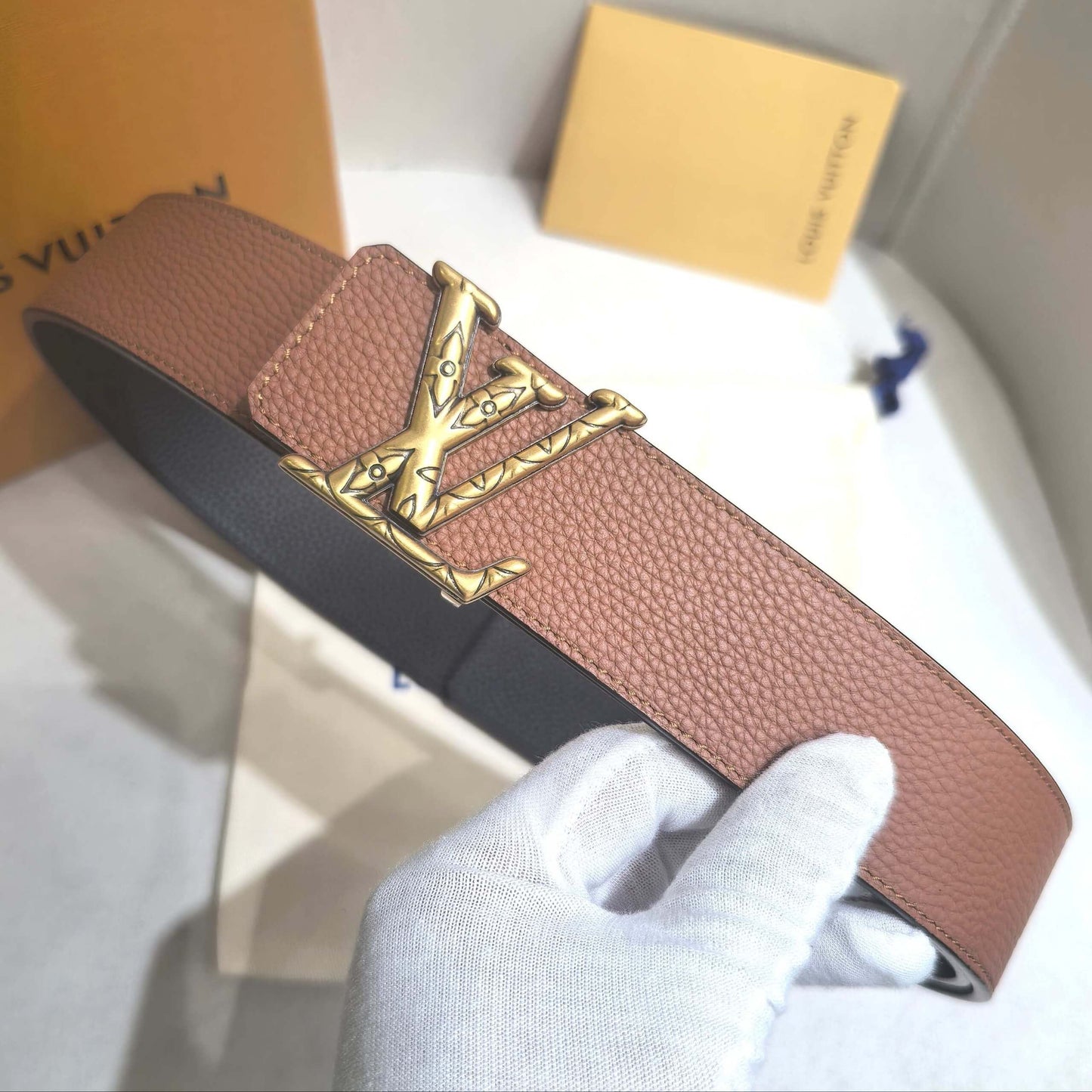 Pink belt with gold buckle held by a gloved hand on a white background