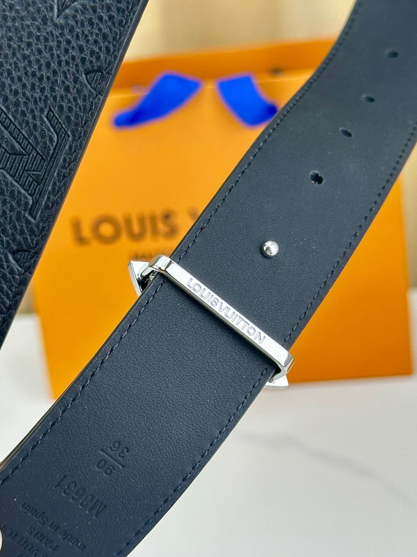 Back leather belt with silver buckle in front of a Louis Vuitton orange box.