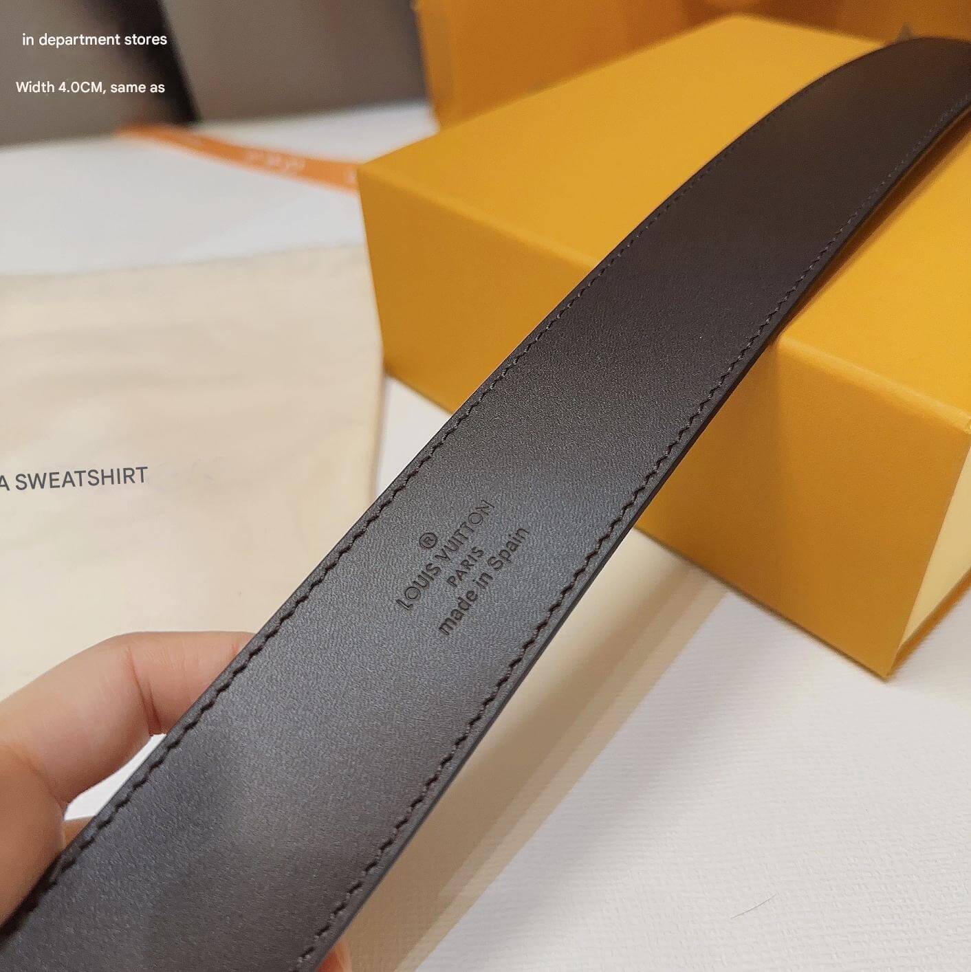 Gray belt with brand logo held by a hand, with a yellow box in the background.