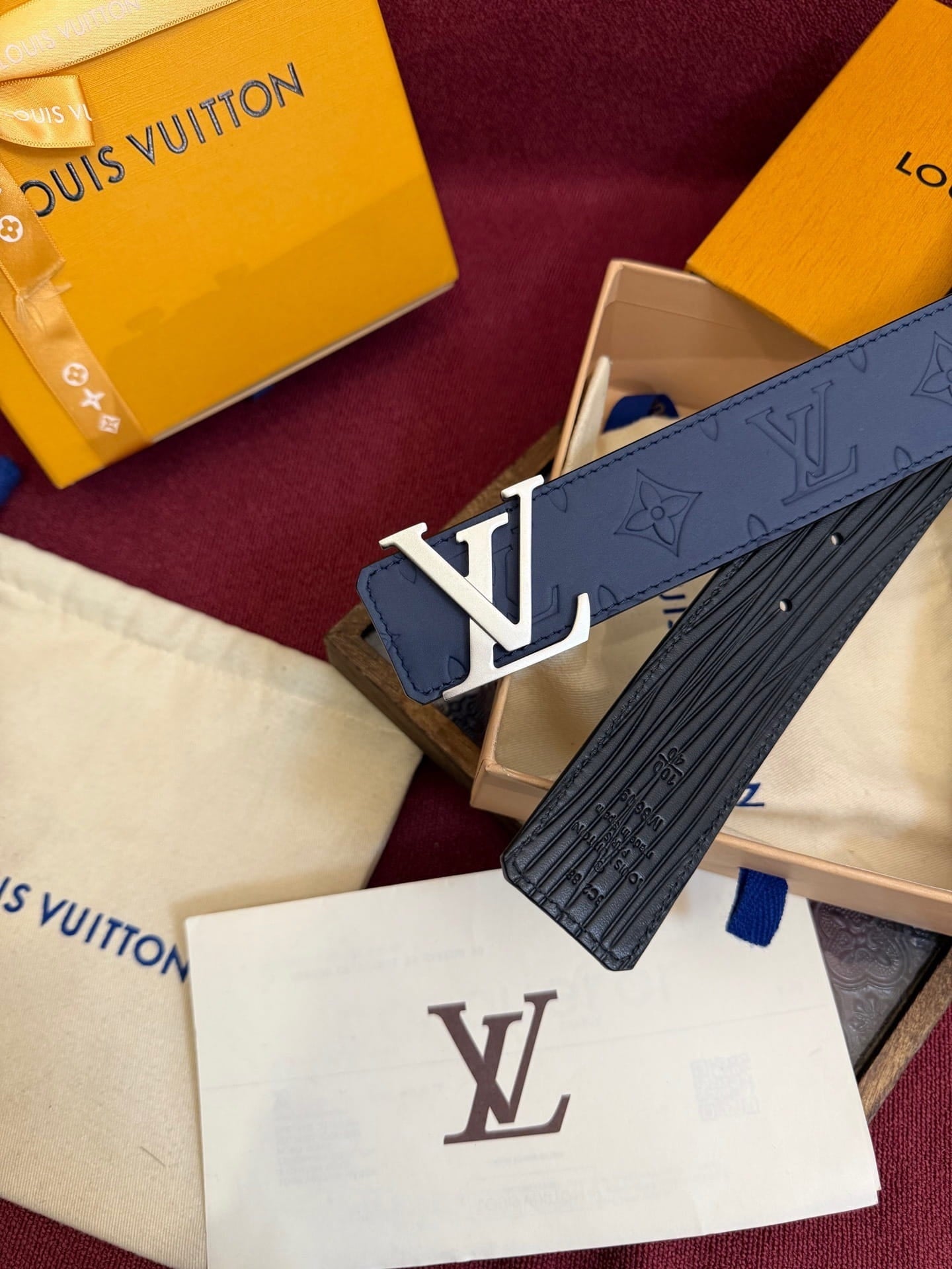 Louis Vuitton belt with packaging and monogrammed paper on a red surface