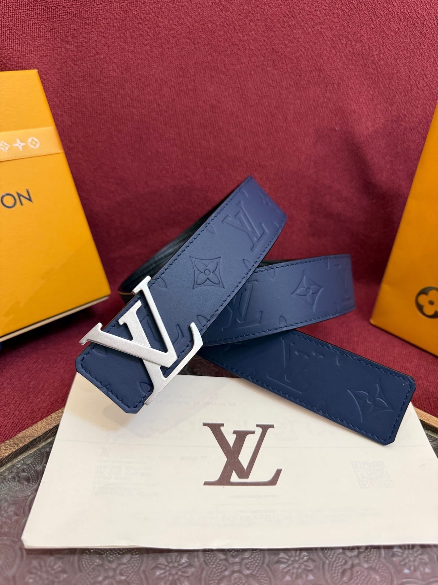 Blue belt with silver buckle on a white pouch with 'LV' logo, against a red background with yellow boxes.