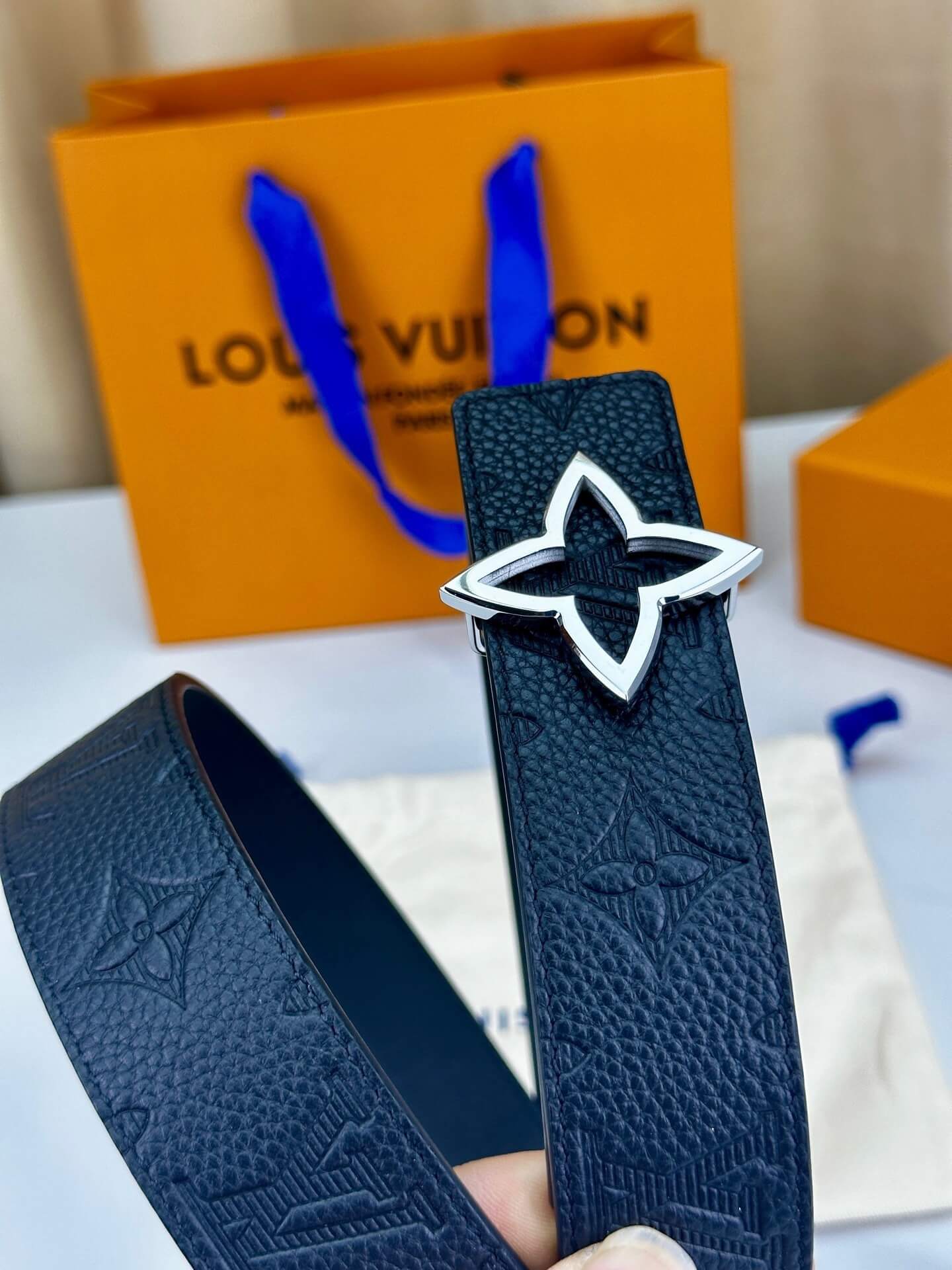 Blue belt with star-shaped buckle held in front of a Louis Vuitton orange bag.