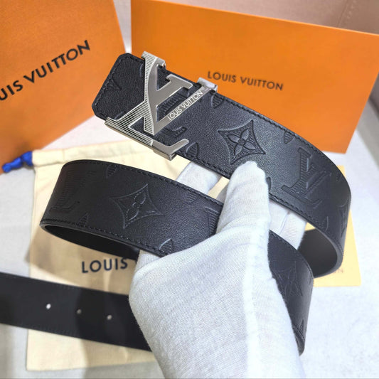Louis Vuitton belt with monogram pattern and silver buckle held by a gloved hand, with brand packaging in the background.