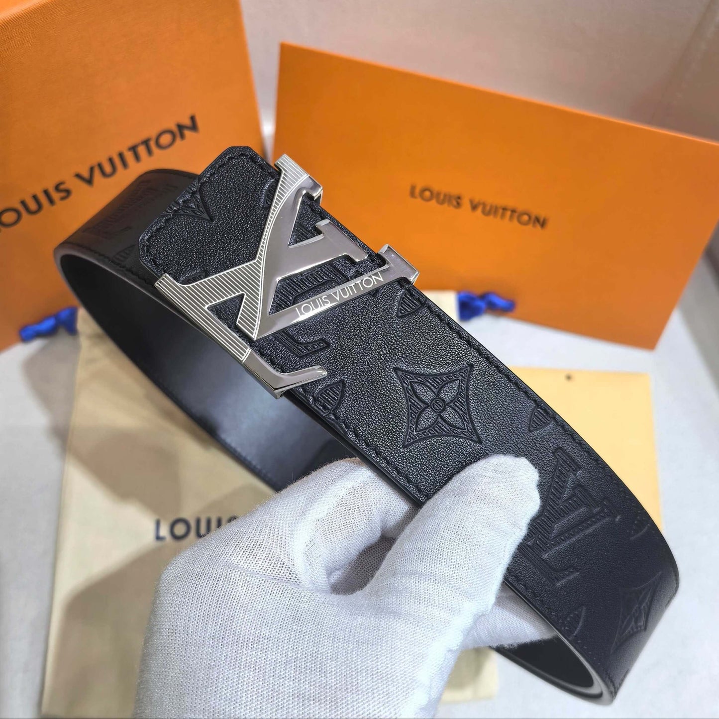 Black Louis Vuitton belt with silver buckle held by a gloved hand, against a branded box background.