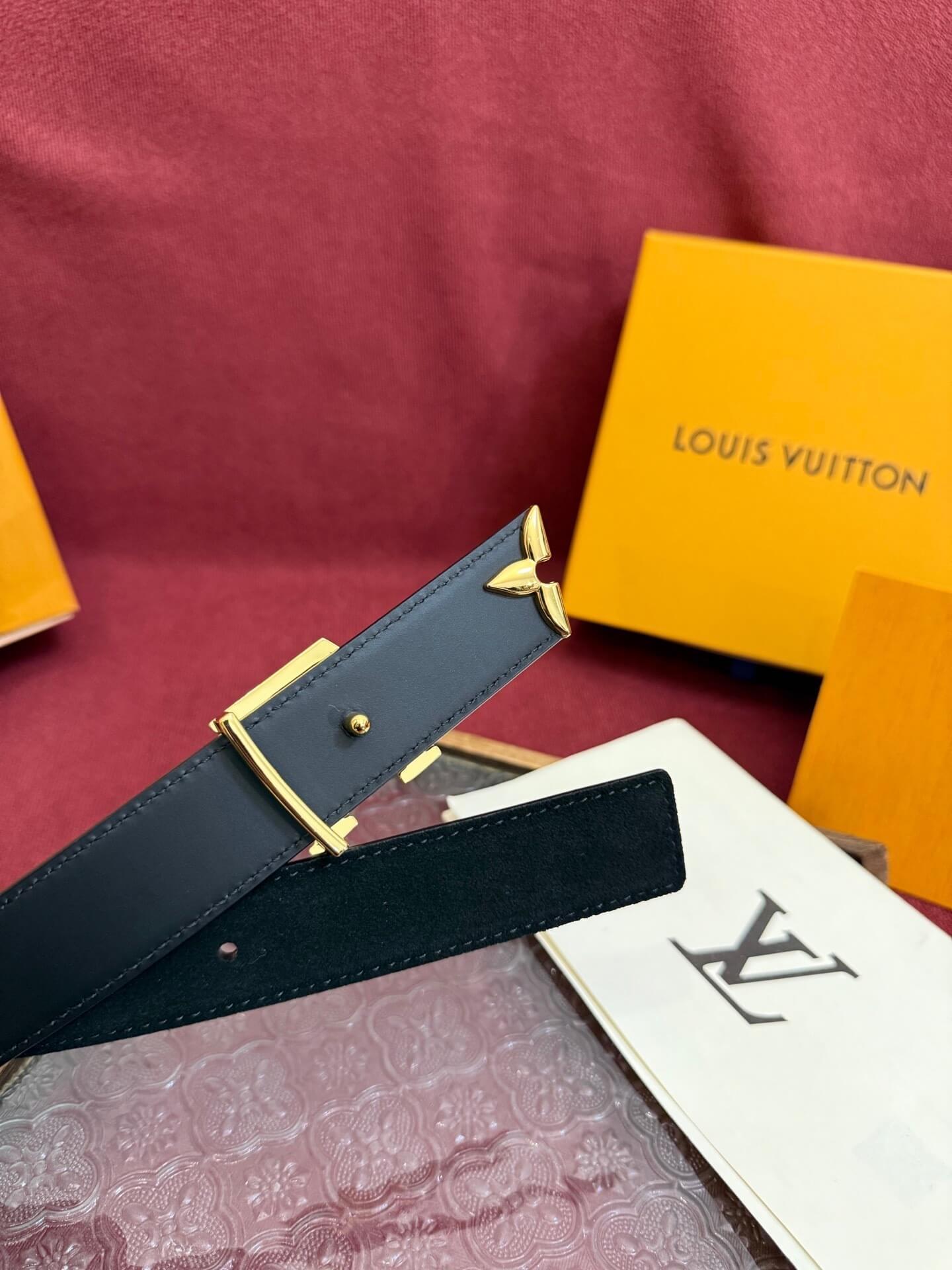 Black belt with gold buckle on a red surface with a Louis Vuitton box.