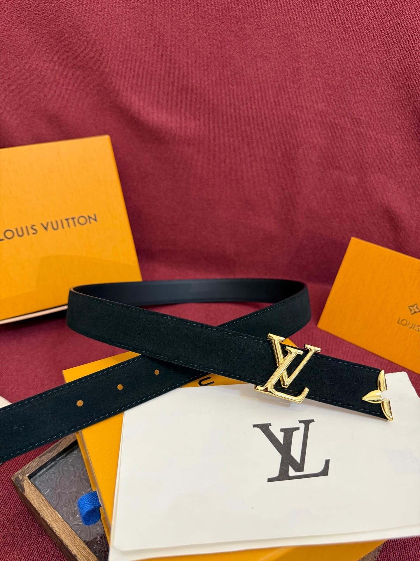 Louis Vuitton belt with gold buckle on a red surface with brand packaging.