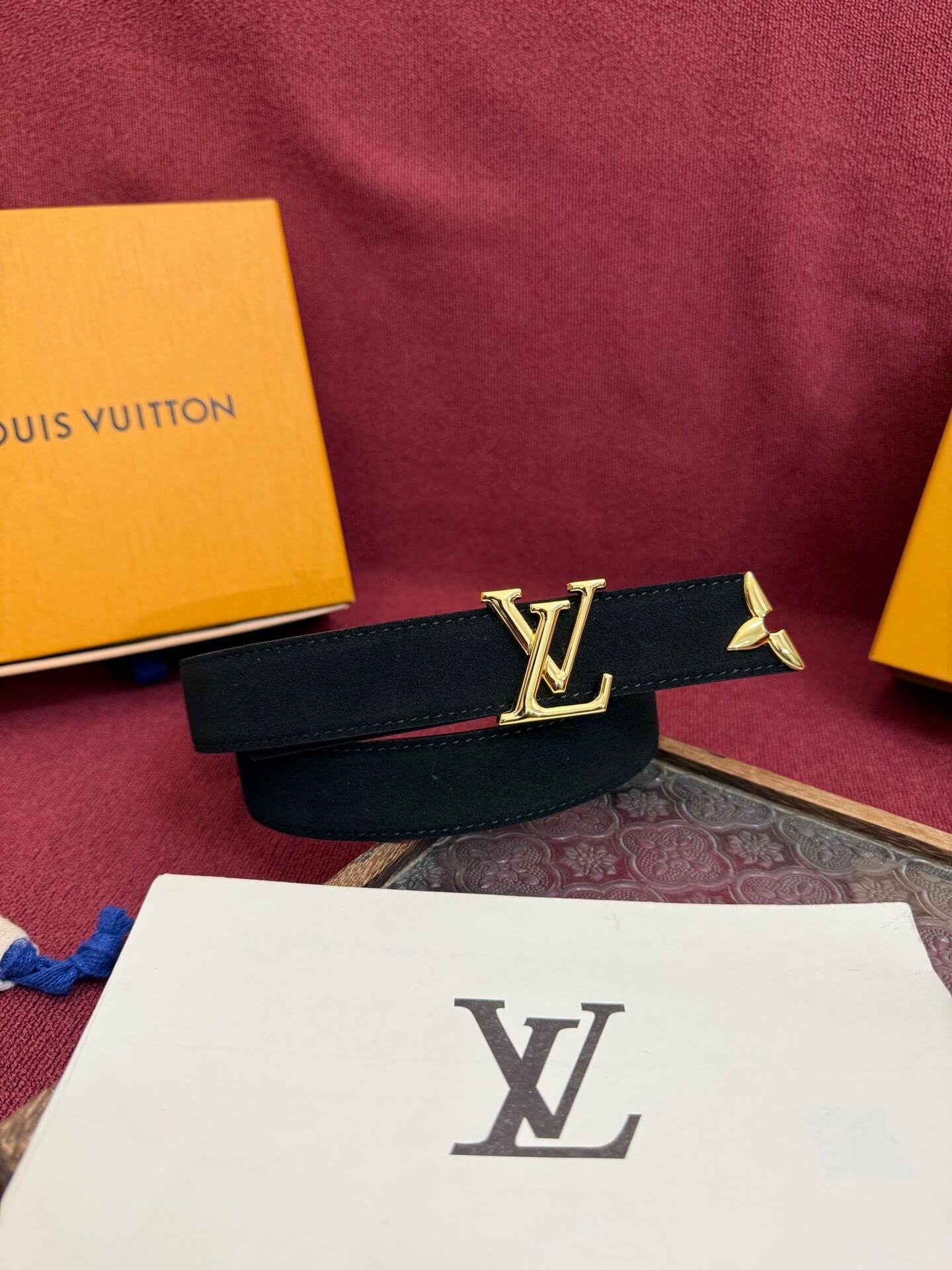 Louis Vuitton belt with gold buckle on a red surface with brand box in the background
