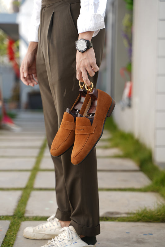 Luxurious Sand Suede Penny Loafers – held by a man in olive trousers, showcasing classic design and relaxed style.