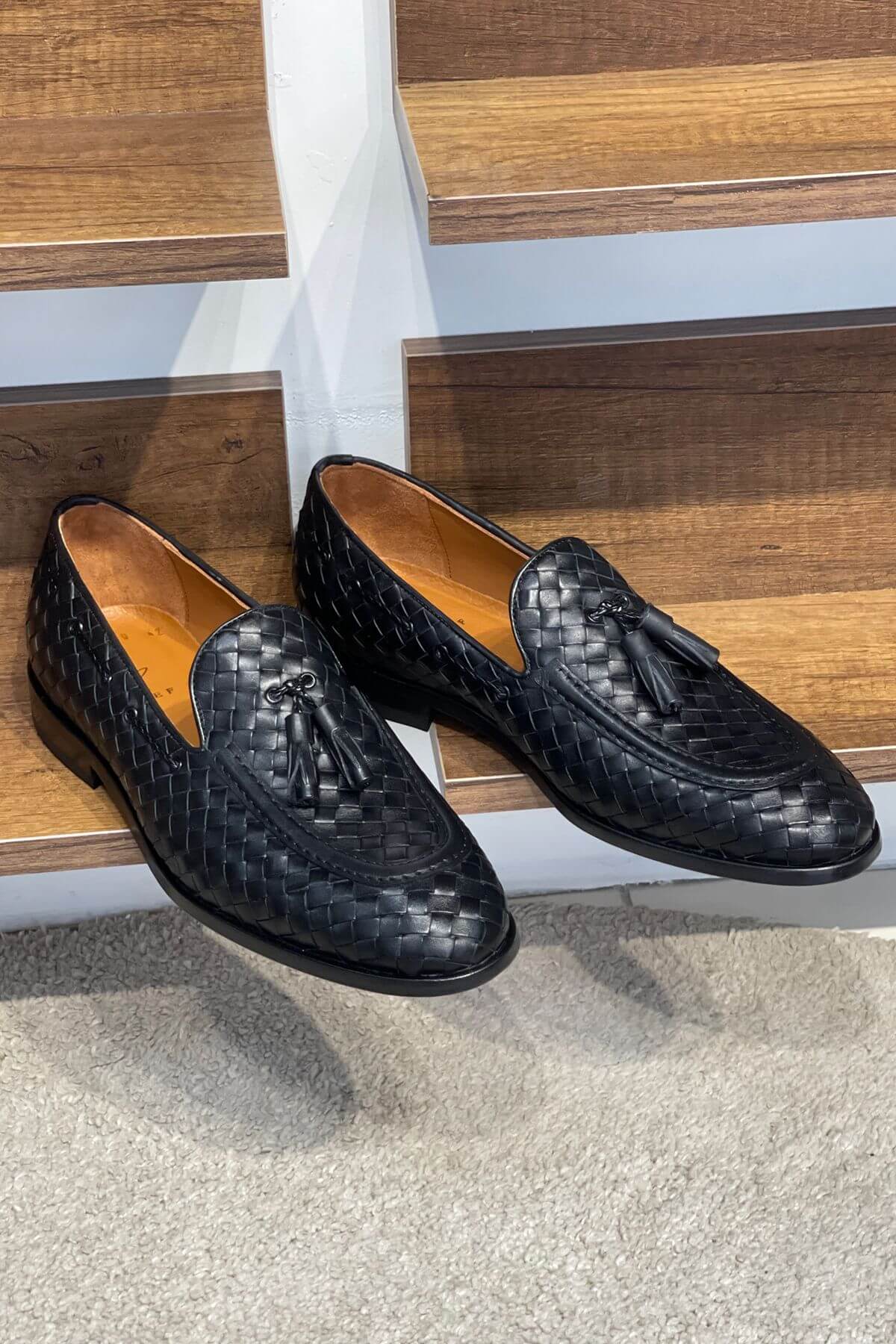 Black woven loafers with tassels on a wooden floor.