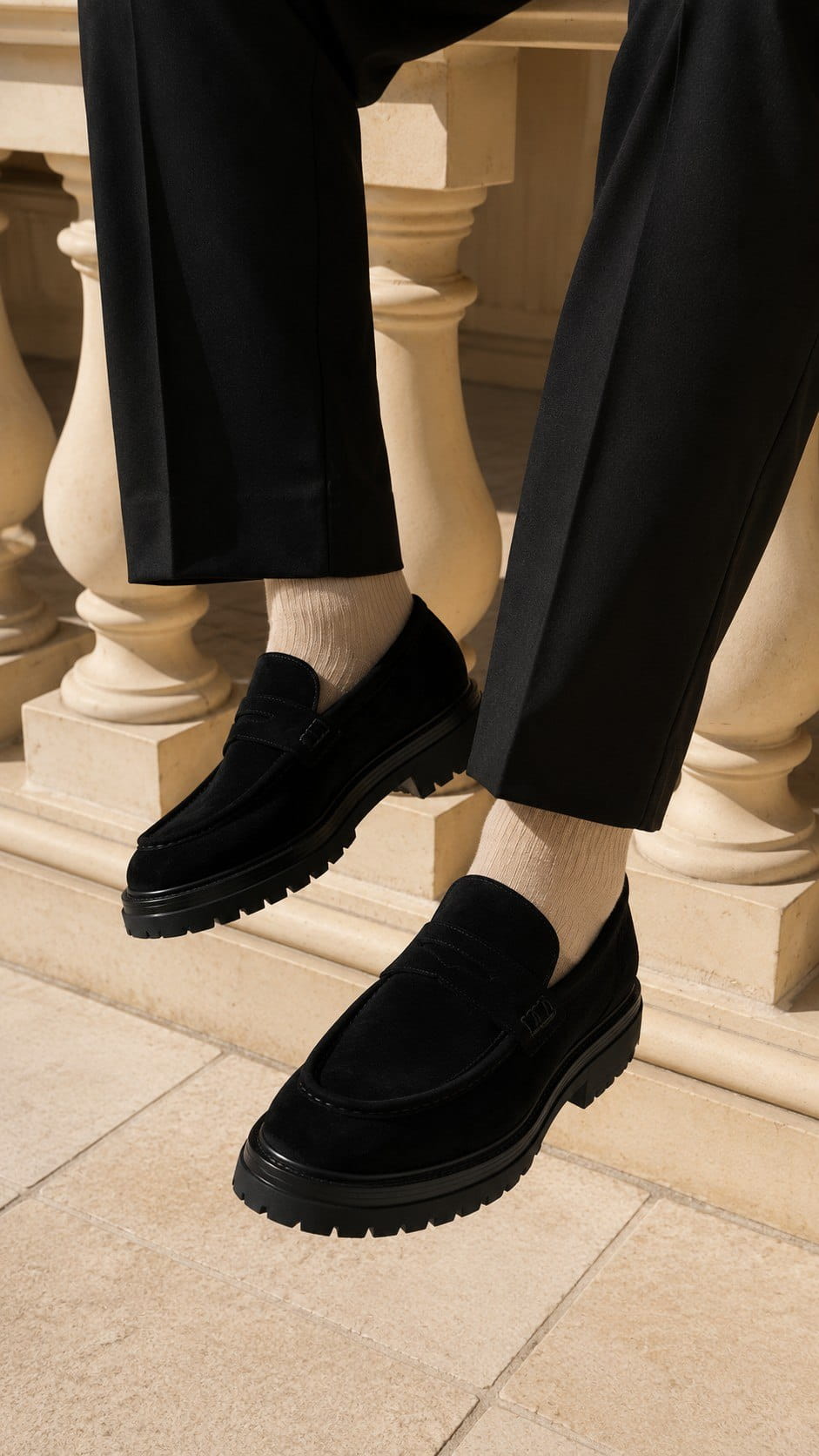 Black loafers worn with black pants and white socks on a stone floor.
