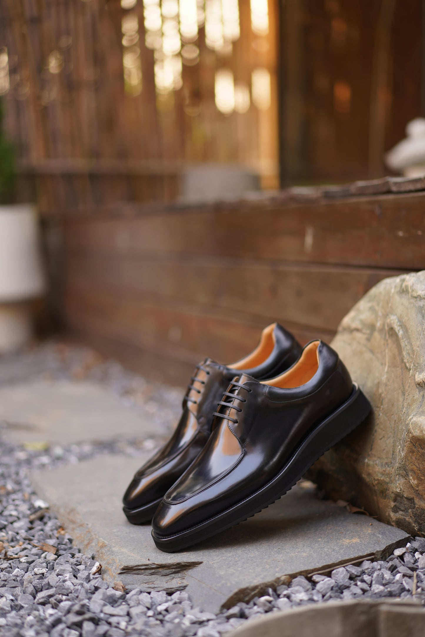 Pair of Black Apron-Toe Derby shoes with high-shine black leather, elevated lug soles, and shoe trees, angled view.