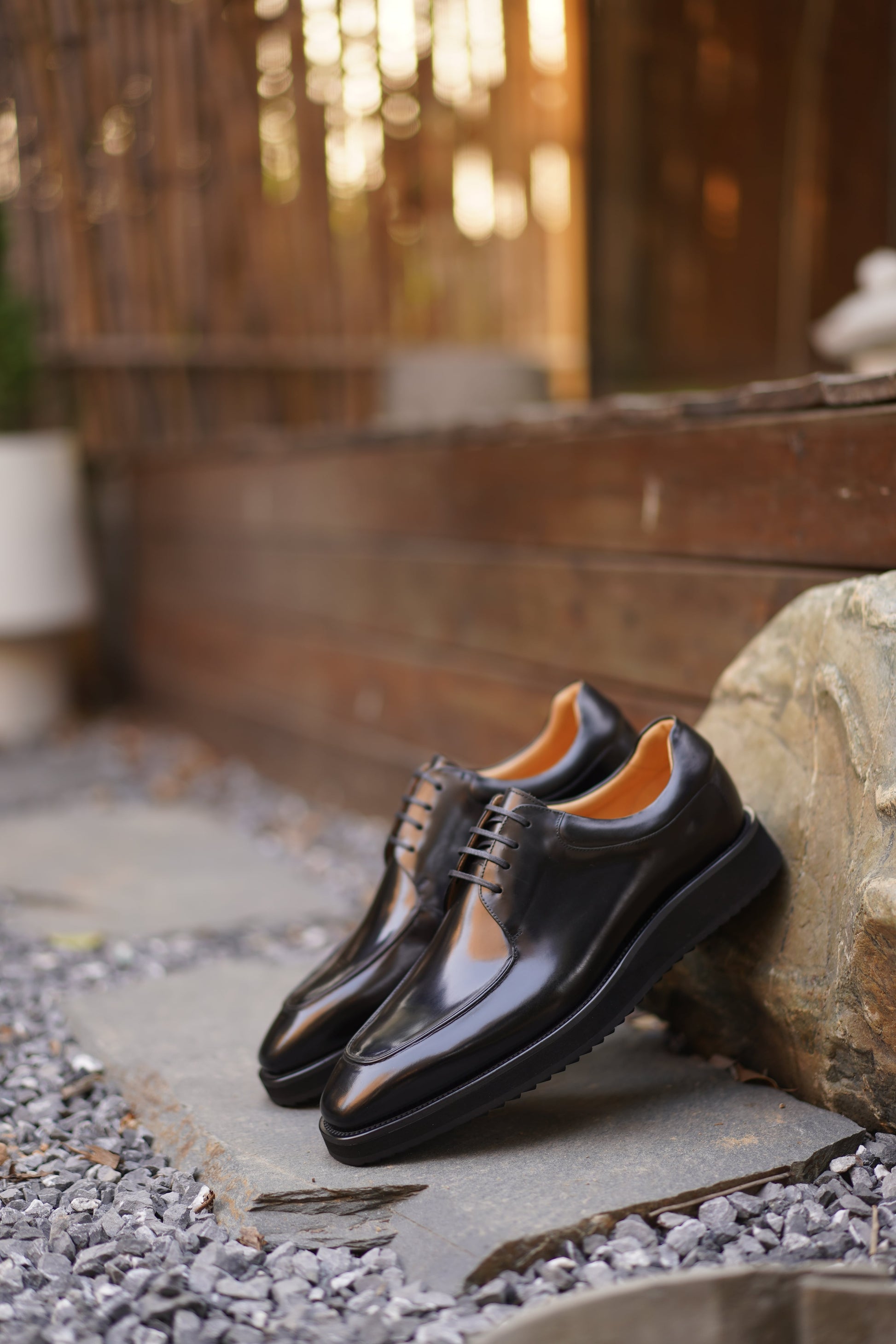 Pair of Black Apron-Toe Derby shoes with high-shine black leather, elevated lug soles, and shoe trees, angled view.
