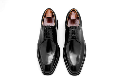 Top-down view of a pair Black Apron-Toe Derby shoe, highlighting the high-shine black leather and elevated lug sole.
