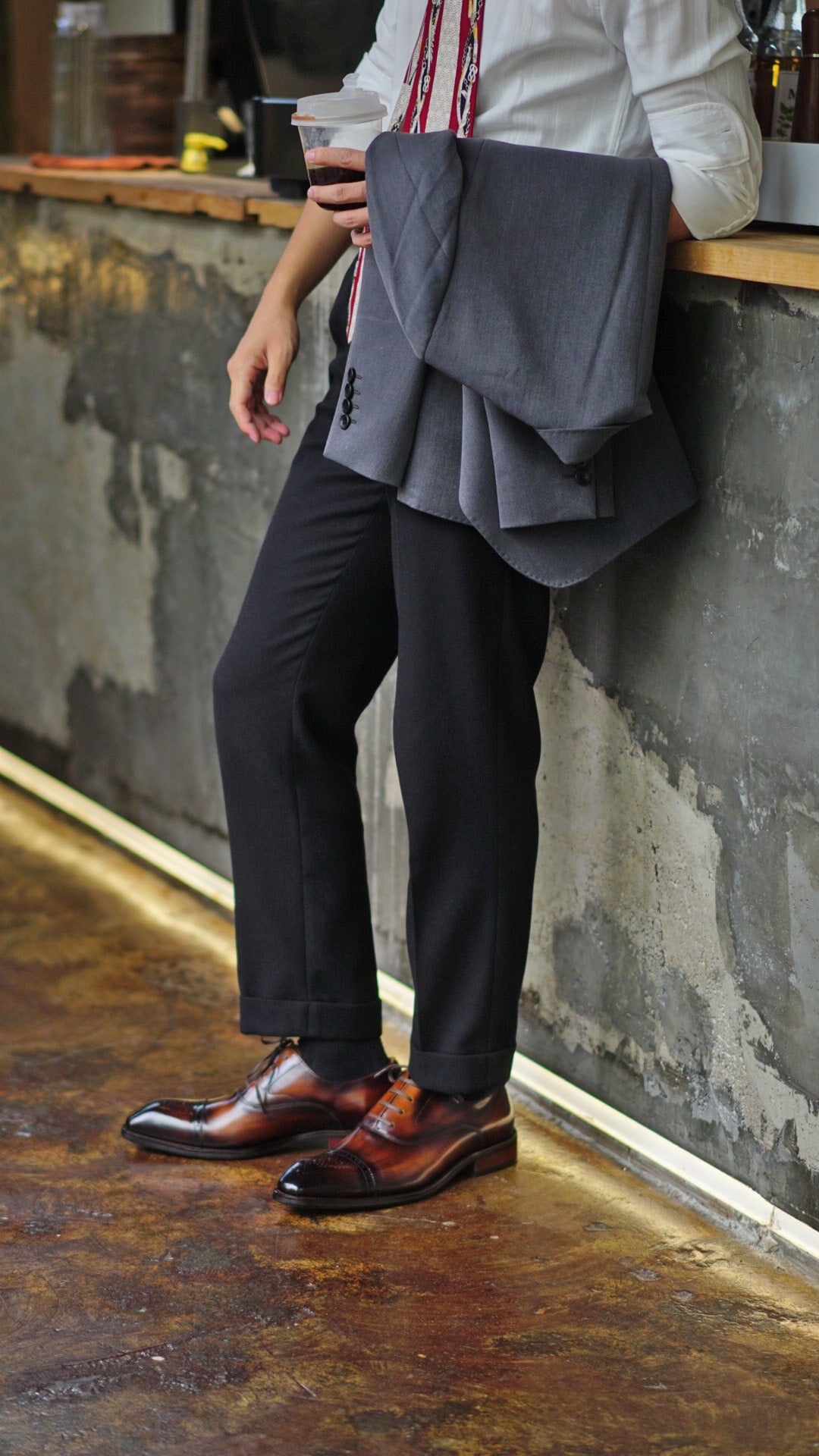 Close-up of men's brown leather Oxford shoes with intricate brogueing and a cap toe, worn with dark trousers.