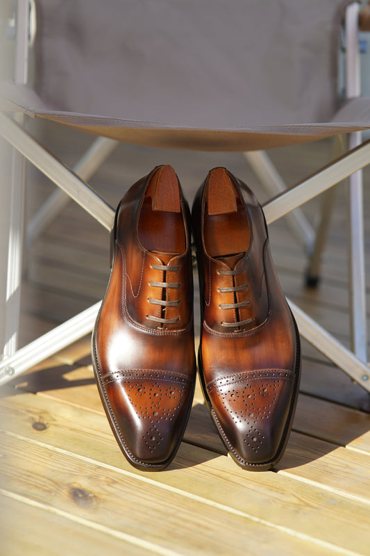 Close-up of men's brown leather Oxford shoes with intricate brogueing and a cap toe.