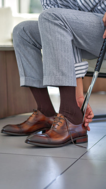 Close-up of men's brown leather Oxford shoes with intricate brogueing and a cap toe.