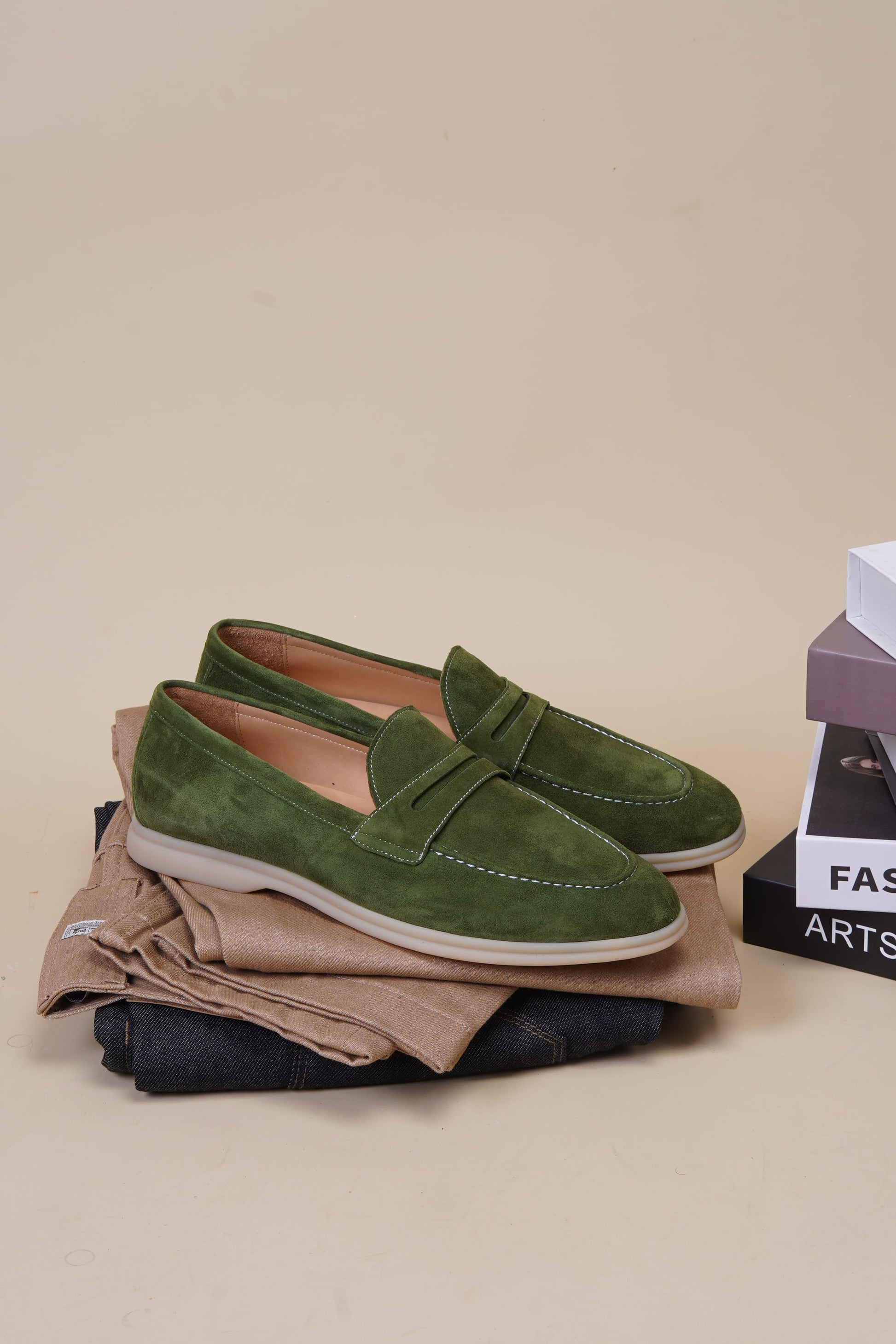 Pair of olive green suede penny loafers styled on neutral surface, side profile