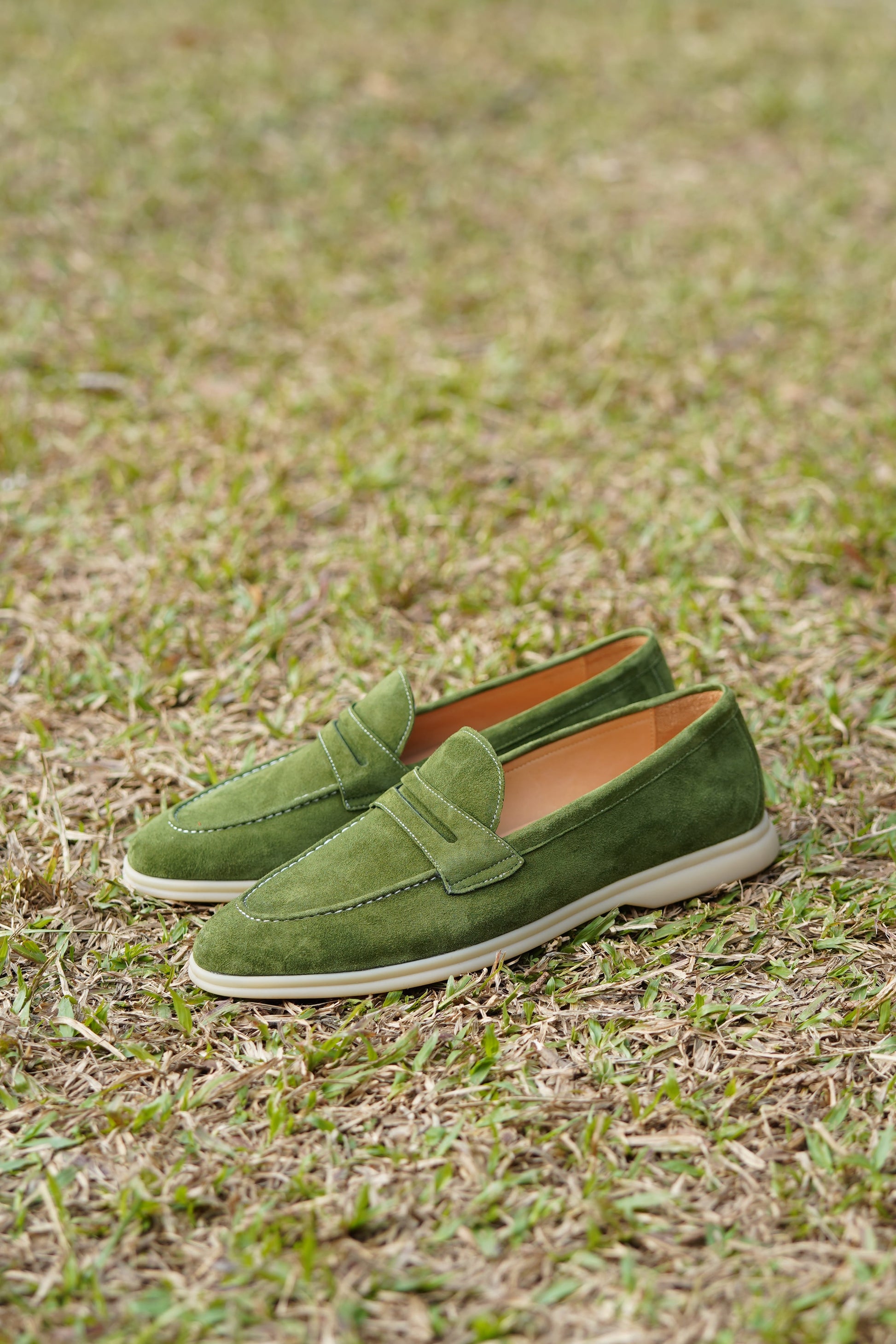 Olive green suede penny loafers on beige background, top view