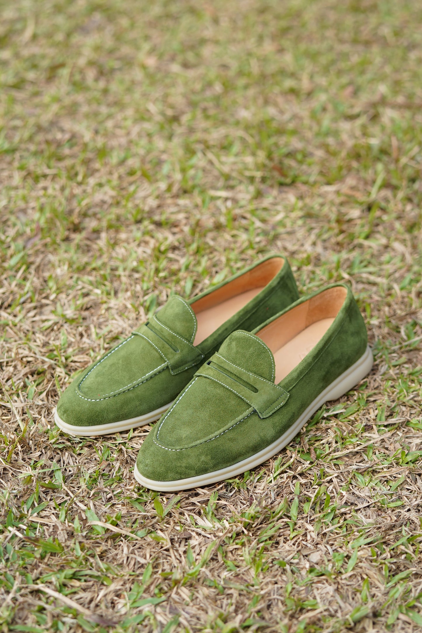Olive green suede penny loafers outdoors on grass, side view