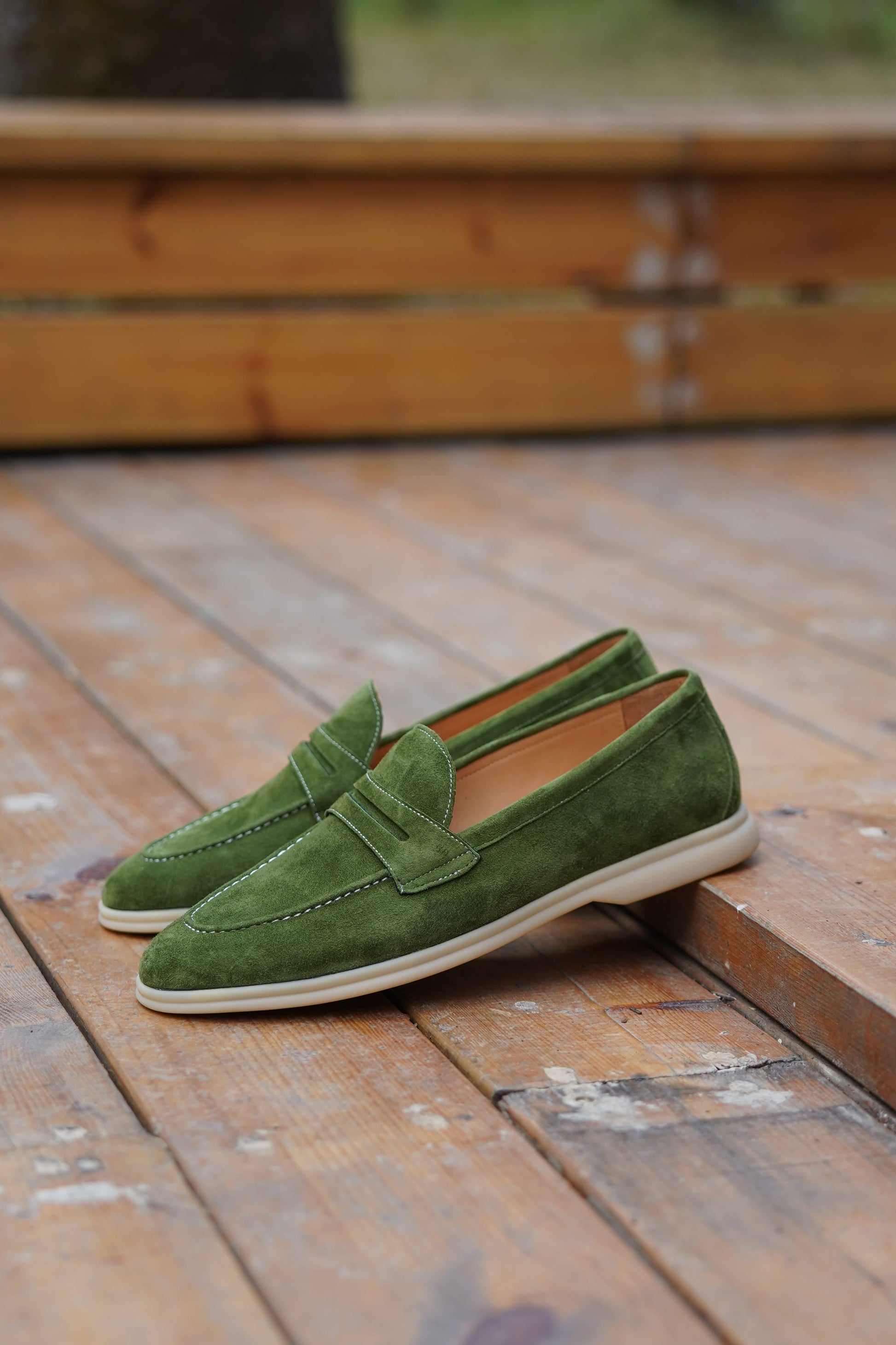 Olive green suede penny loafers on a wooden surface, angled view