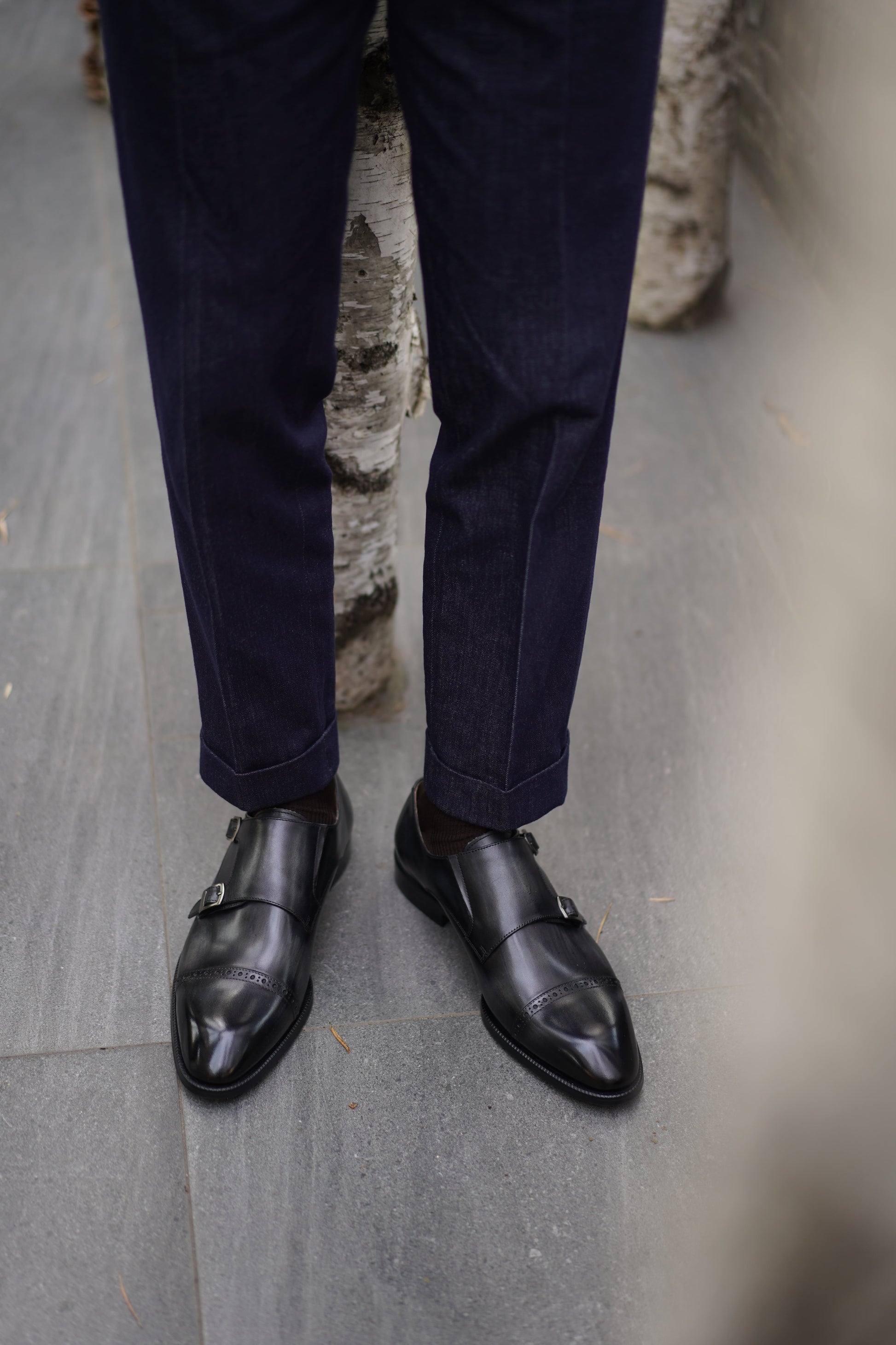 Polished Black Double Monk Strap Leather Shoes – worn by a man in cuffed dark blue trousers, showcasing their sleek appearance and modern formality.