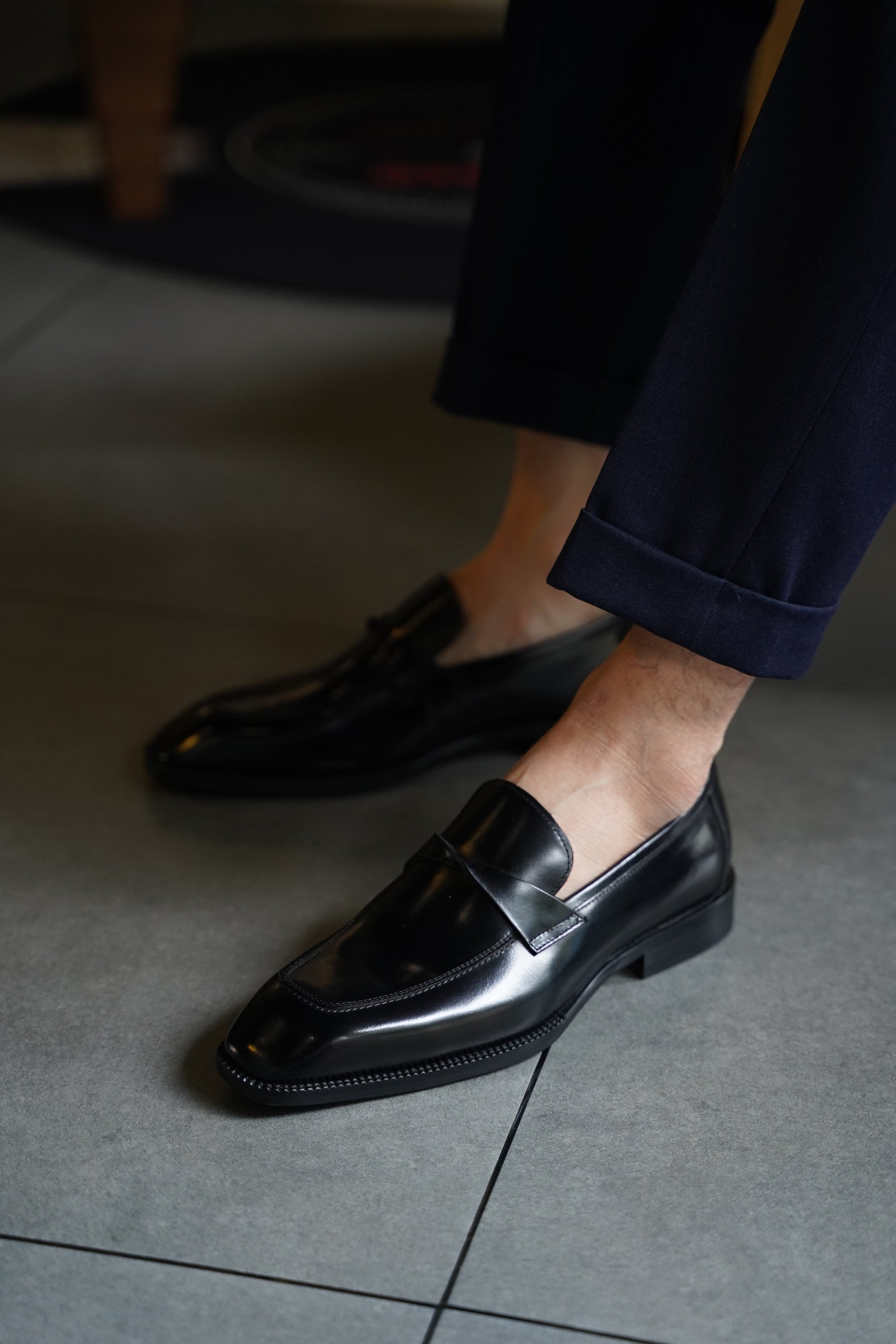 Polished Black Leather Slip-On Loafers for Formal & Semi-Formal Wear – worn by a man in cuffed navy trousers, highlighting the sleek silhouette and polished finish for formal occasions.