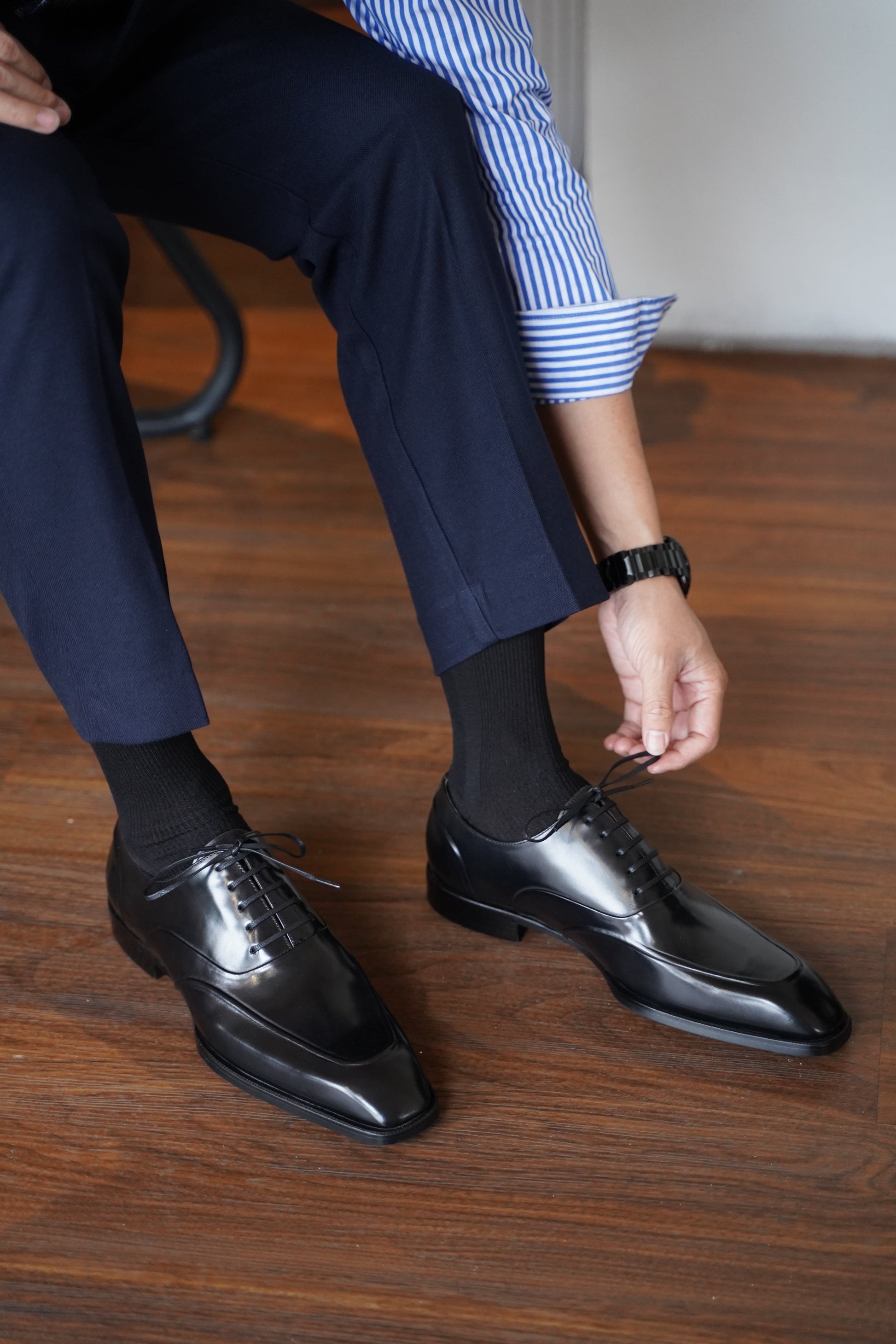 Model tying handcrafted black split-apron Oxford dress shoes – luxury leather footwear in natural lighting