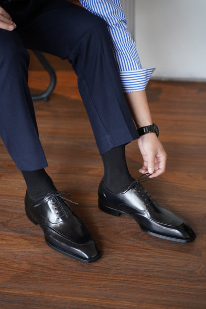 Model tying handcrafted black split-apron Oxford dress shoes – luxury leather footwear in natural lighting