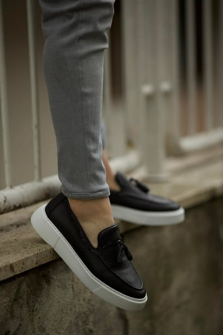 Premium Black Tassel Slip-Ons for Casual & Semi-Formal Wear – worn by a man in grey trousers, standing on a ledge, showcasing premium leather and a versatile design. 