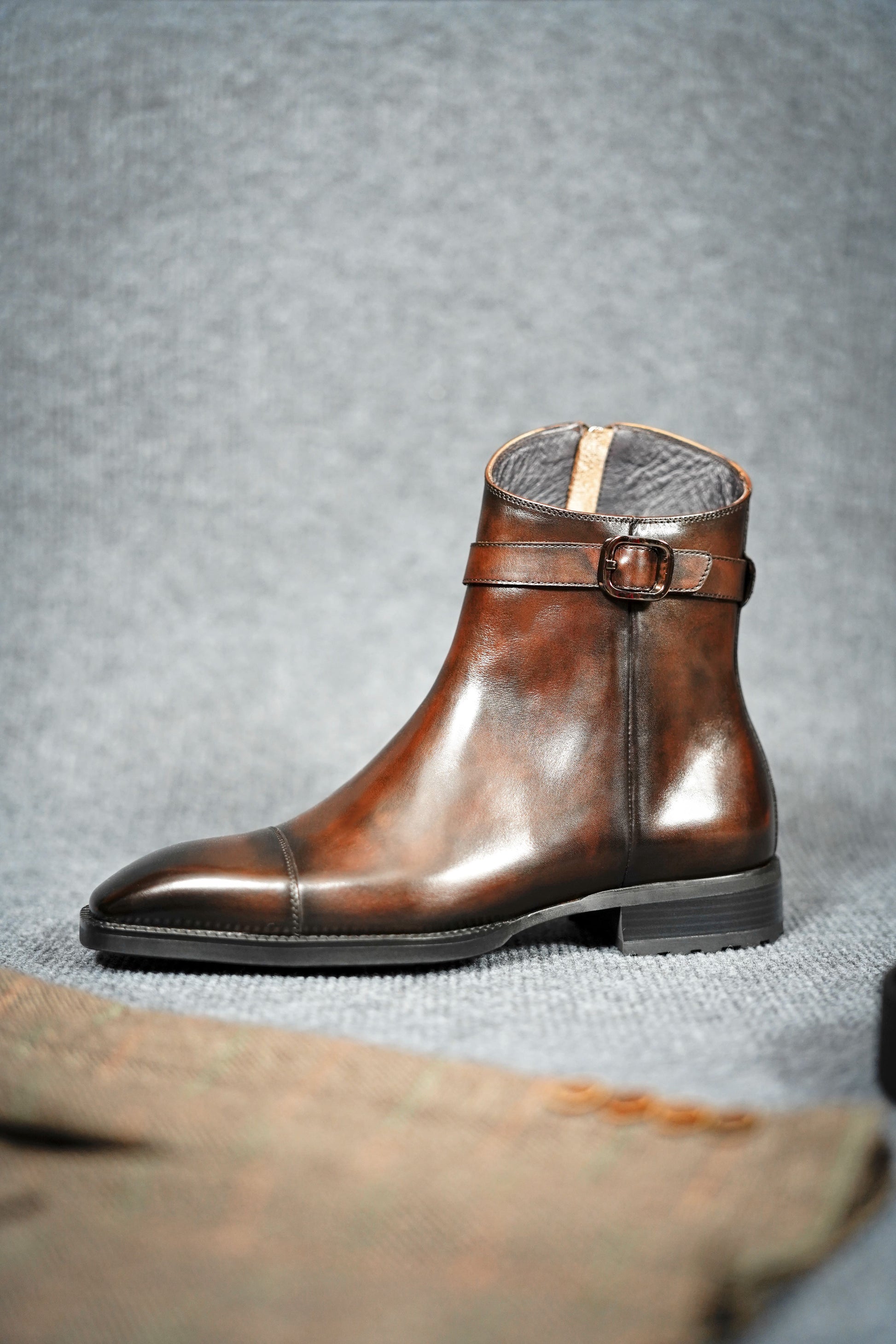 Premium Brown Leather Ankle Boots for Urban Adventures – a side view of a single brown leather boot with a buckle, on a textured gray background.