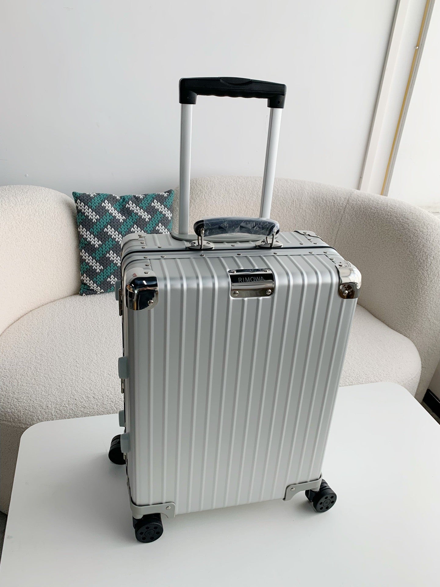 Silver suitcase on a white surface with a light gray couch and patterned pillow in the background
