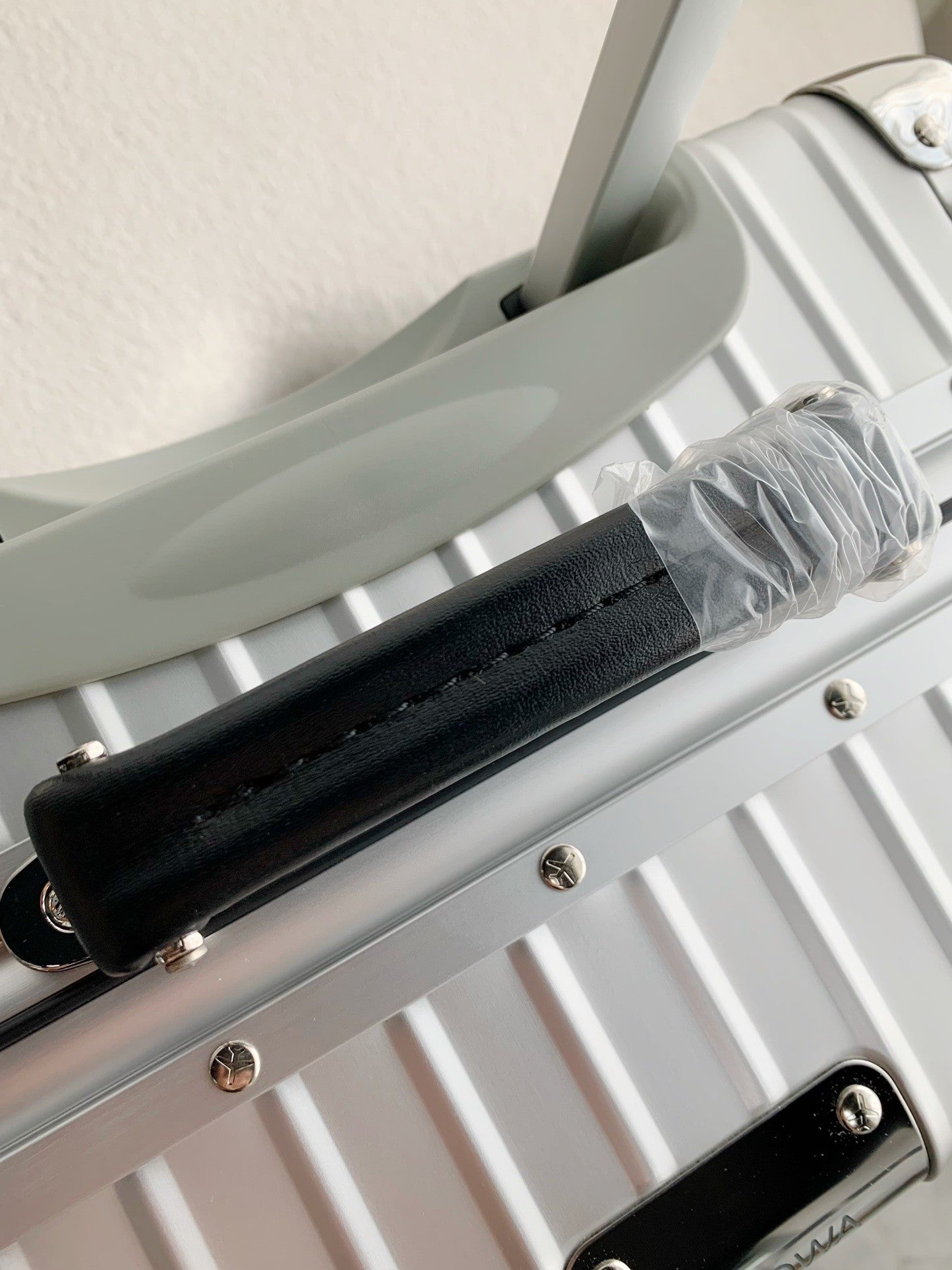 Silver suitcase with a black handle and clear plastic wrap on a white background