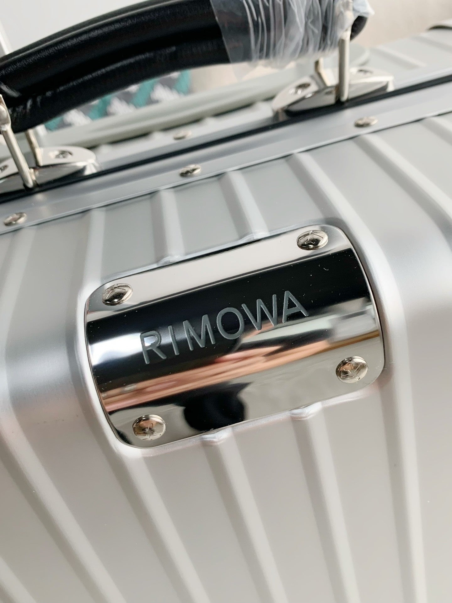 Silver suitcase with a chrome plaque displaying 'RIMOWA' on a blurred background