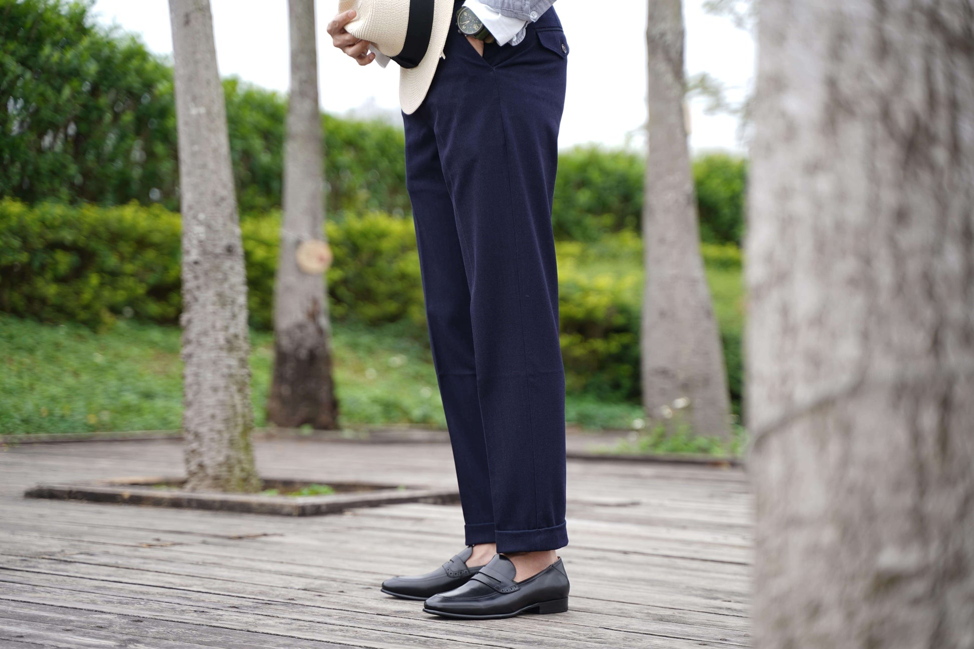 Refined Black Leather Penny Loafers – worn by a man in navy cuffed trousers, standing on a wooden deck, highlighting timeless elegance and a polished finish.