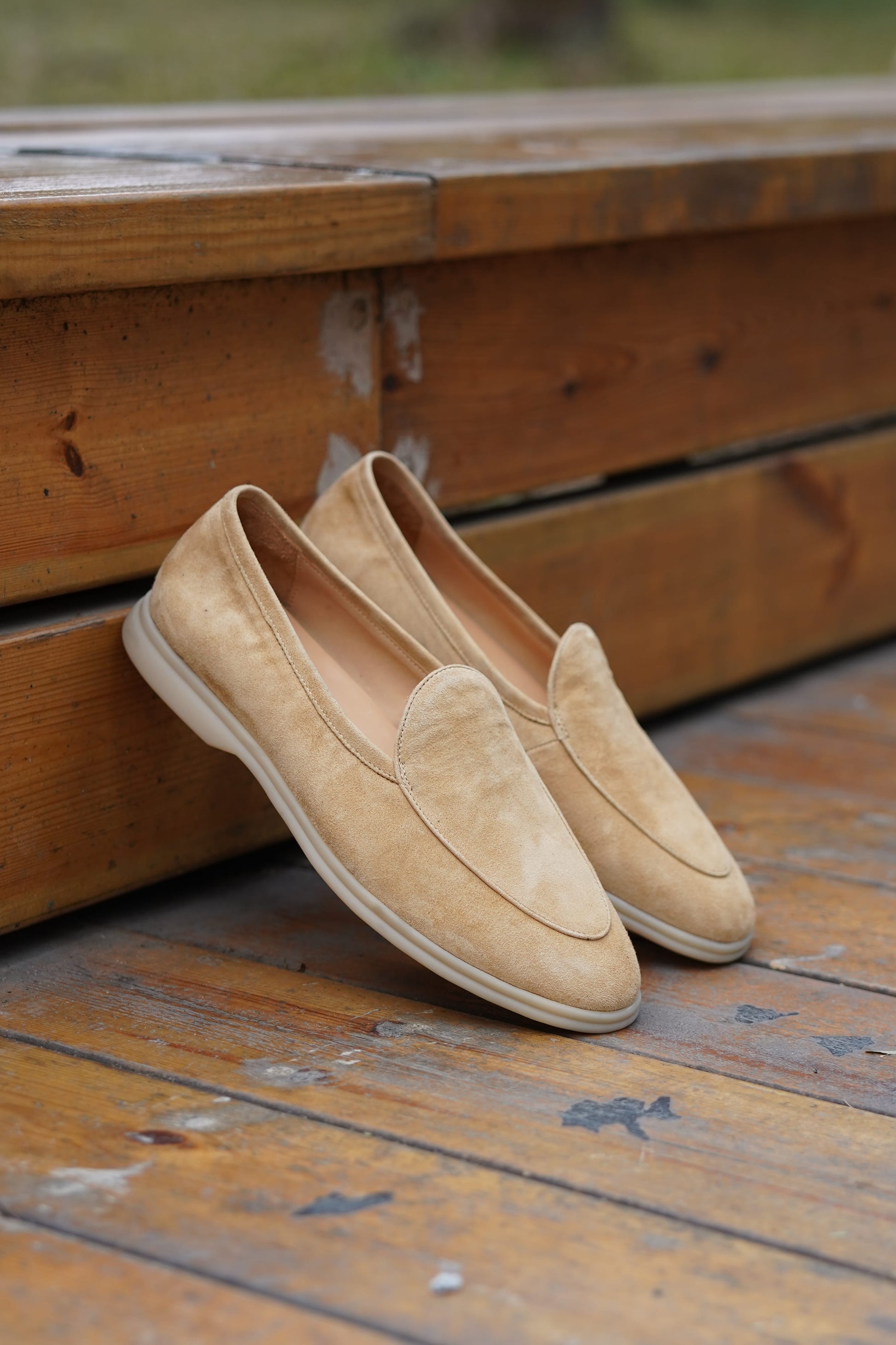 Desert-sand suede Venetian loafers on a wooden surface, angled view