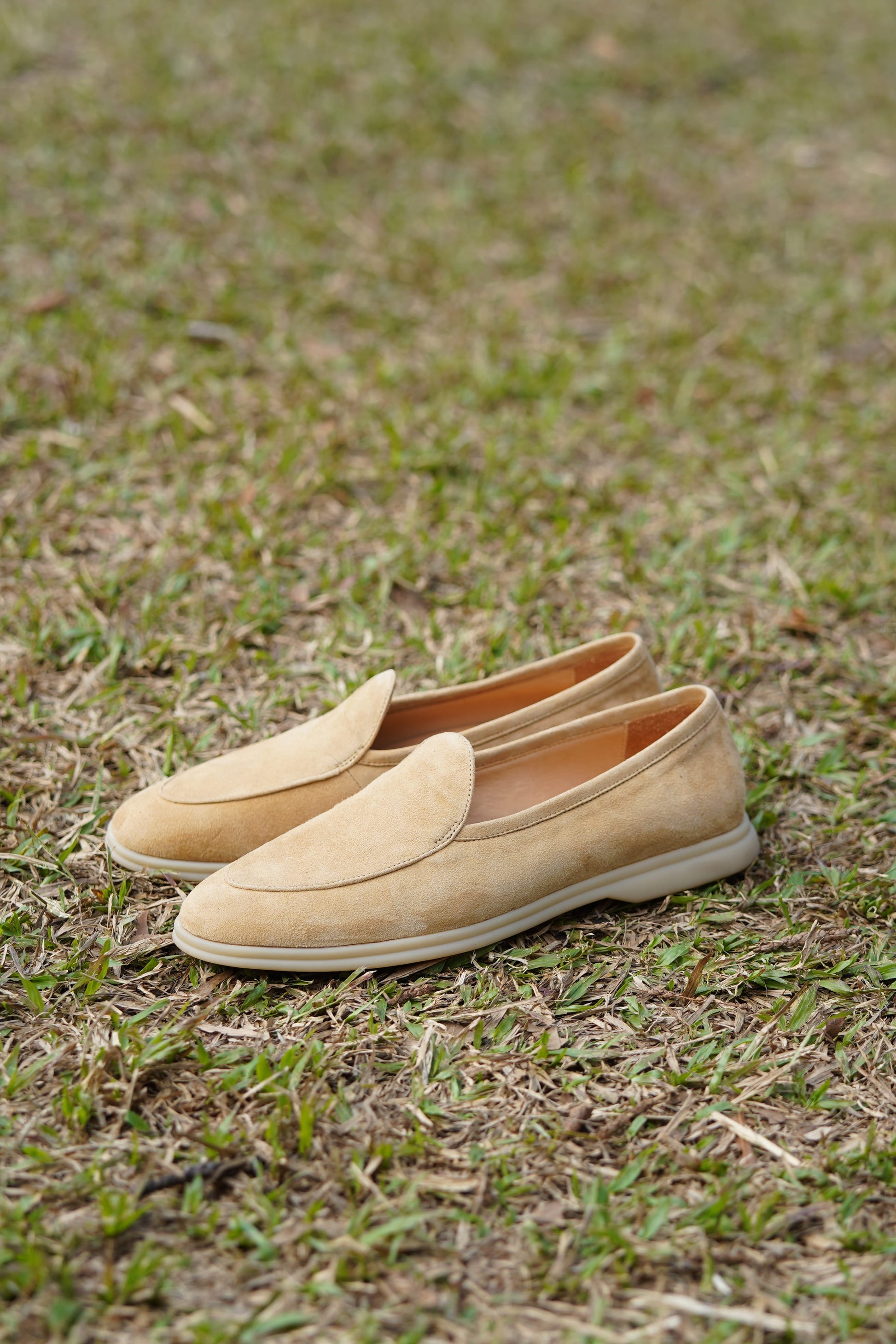 Desert-sand suede Venetian loafers on grass, outdoor side view