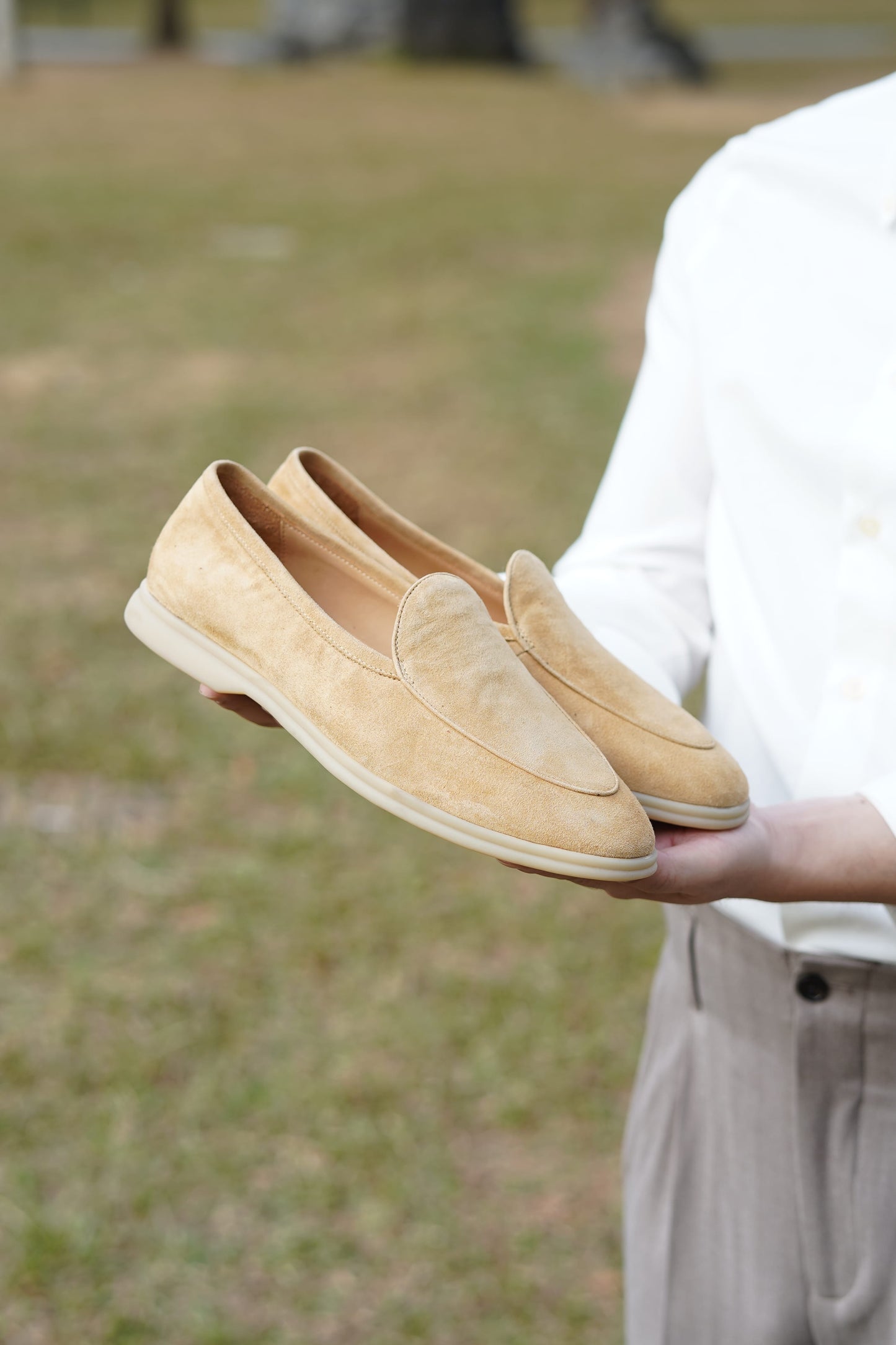 Capri tan suede slip-on loafers held against greenery, clean vamp detail