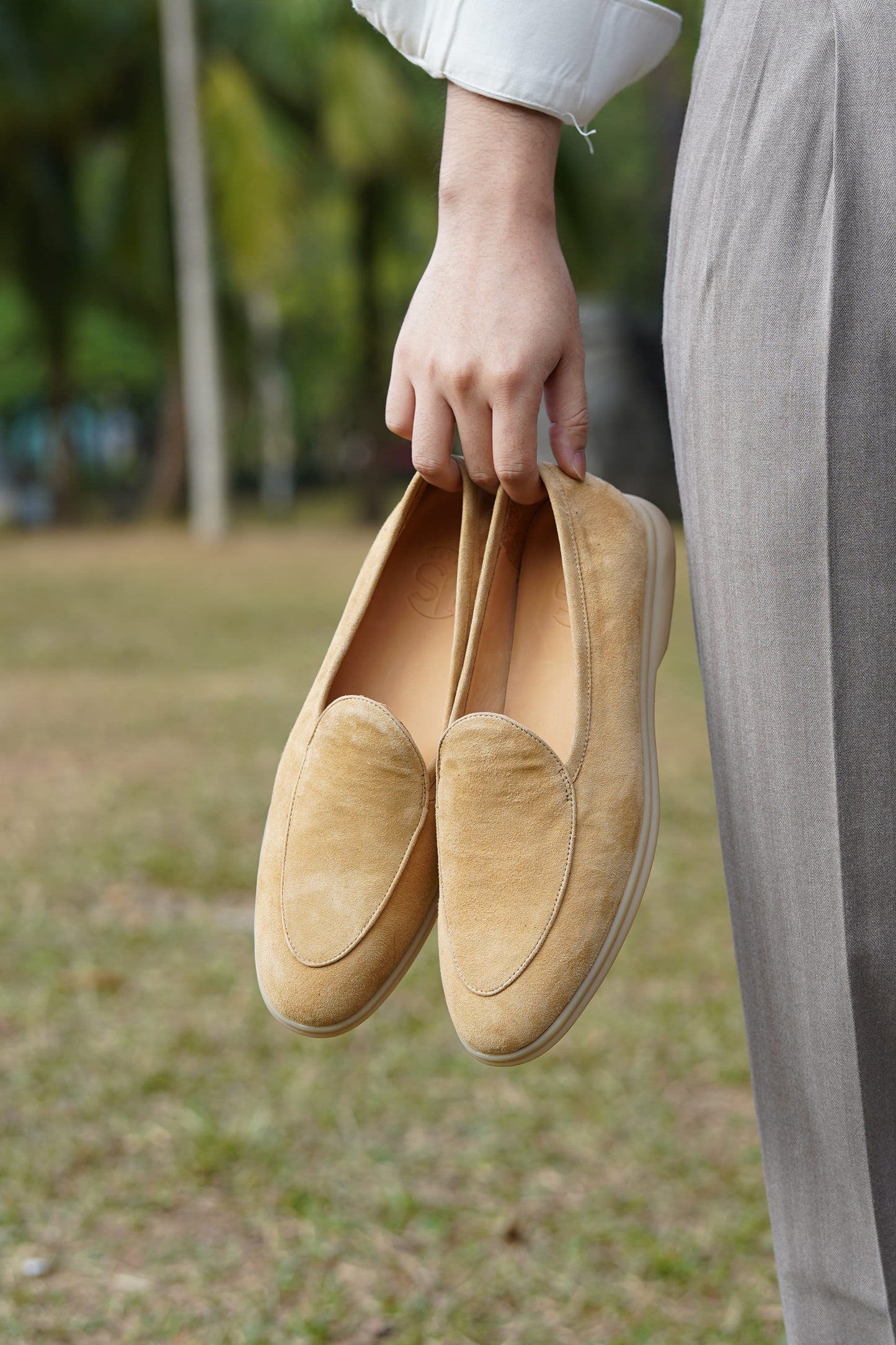 Hand holding Capri tan suede Venetian loafers outdoors, three-quarter view