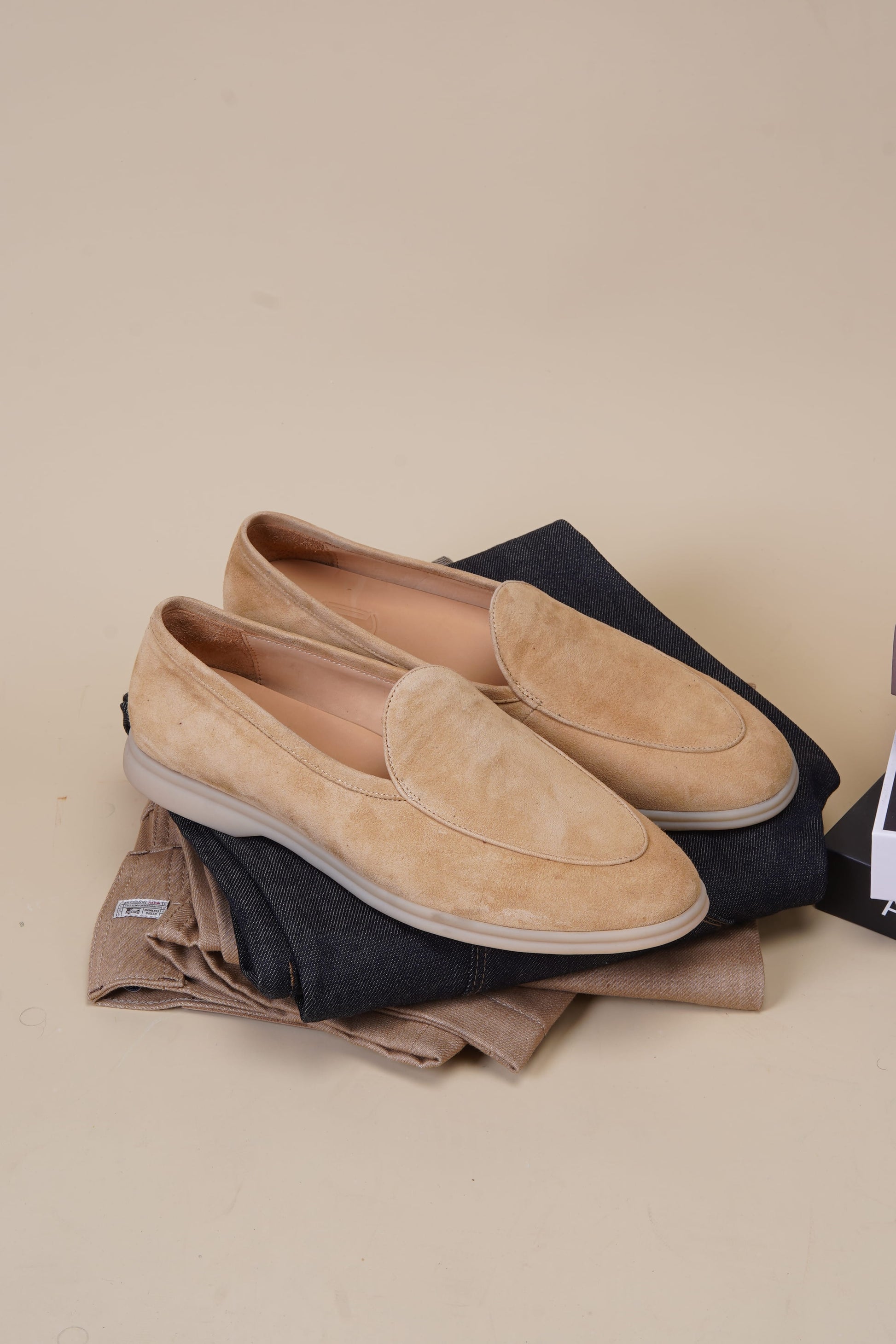 Pair of Capri desert-sand suede Venetian loafers on beige background, top view