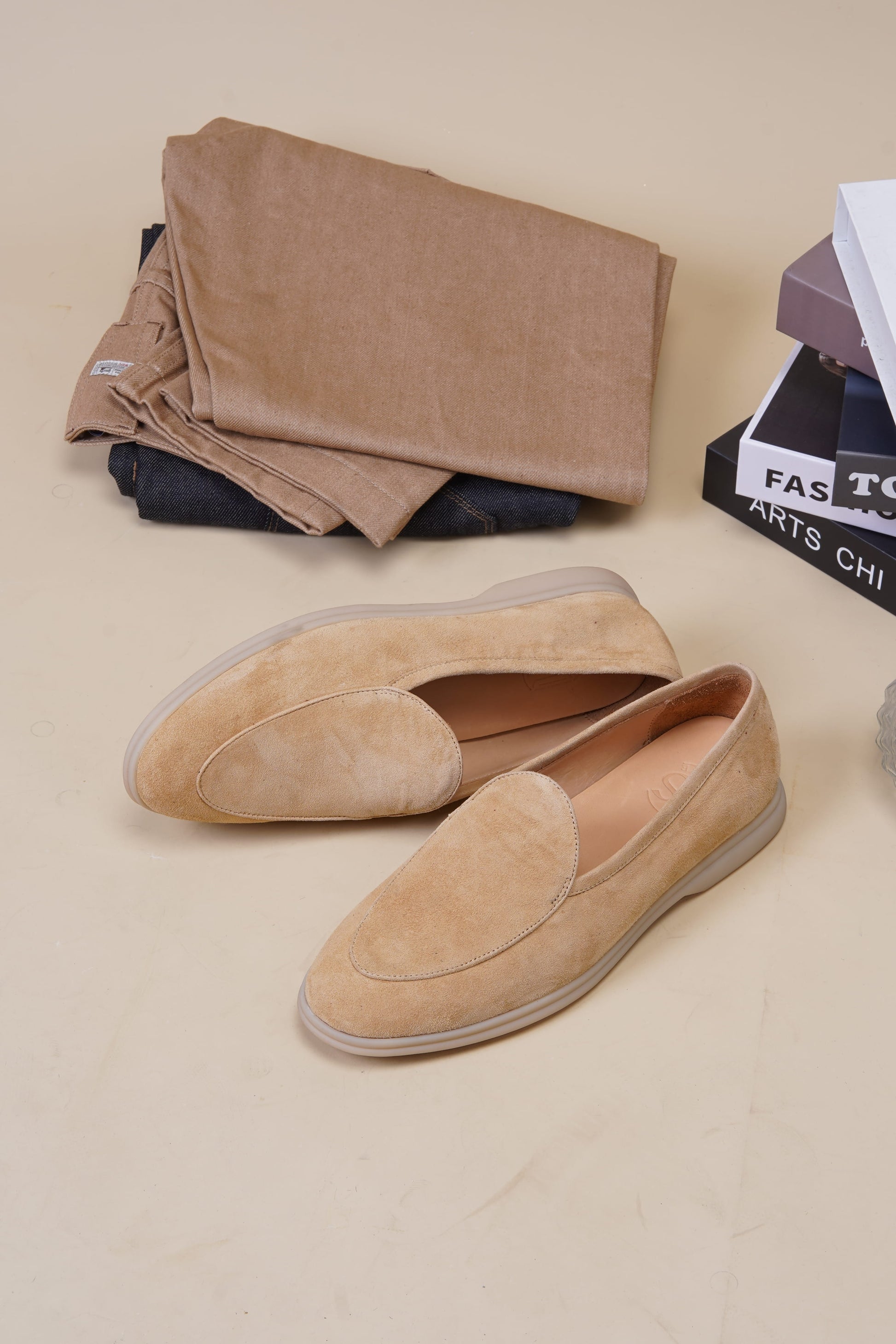 Tan suede Venetian loafers on neutral surface with folded fabric, side profile