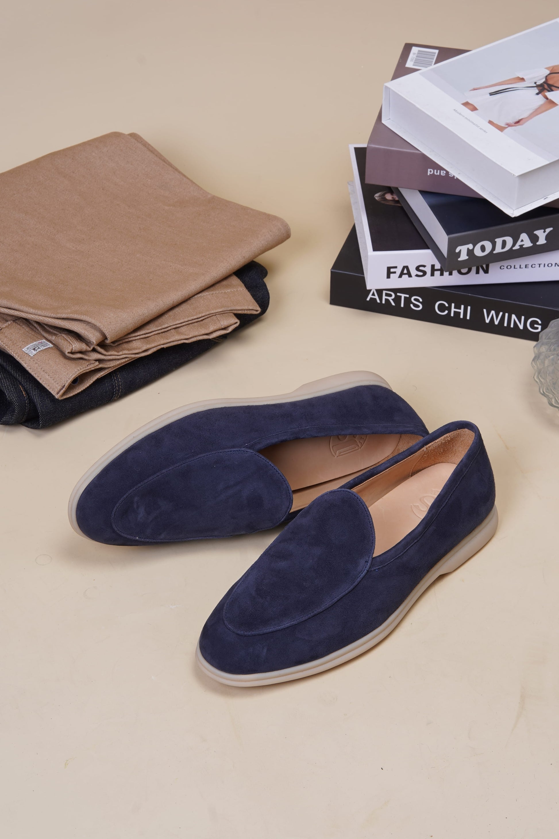 Navy blue suede Venetian loafers on beige surface with books, side profile