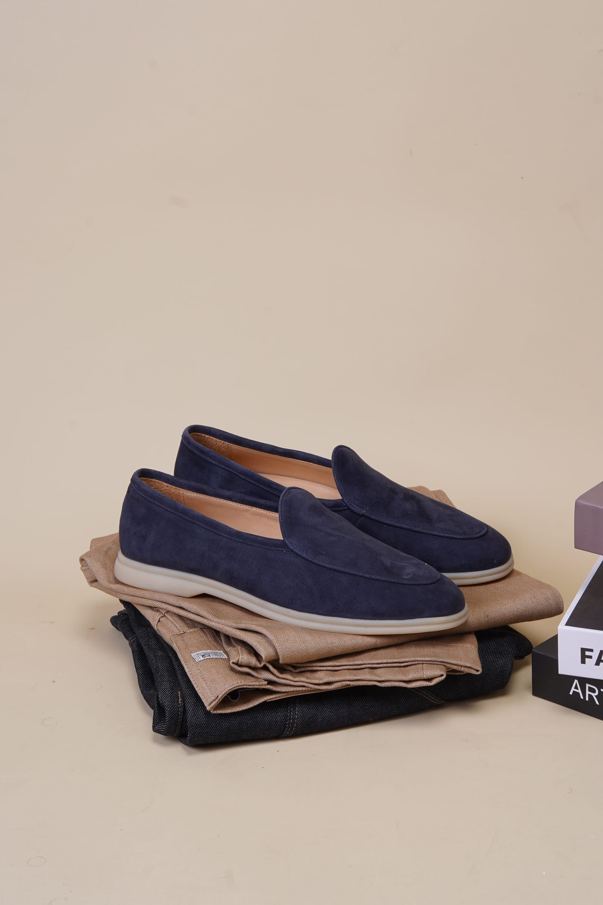 Navy blue suede Venetian loafers styled on folded clothes, neutral background