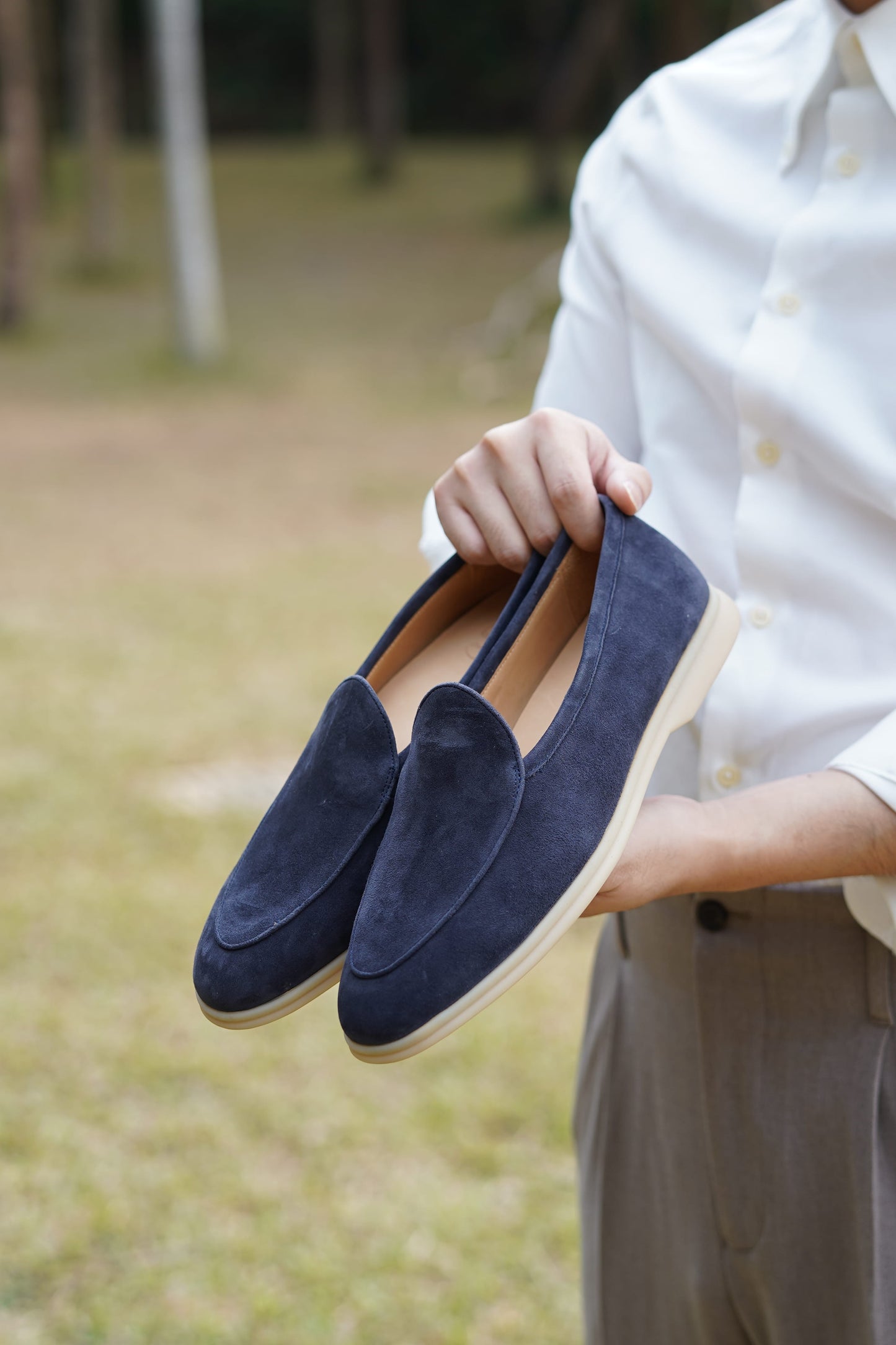 Hand holding Portofino navy blue suede Venetian loafers outdoors, three-quarter view